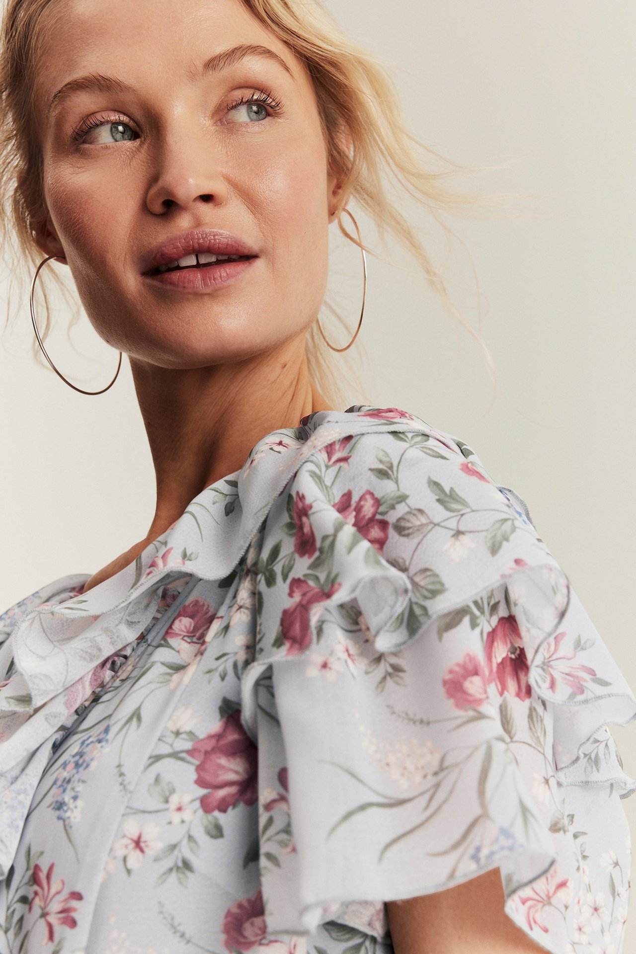 Nahaufnahme einer Frau in einem hellblauen geblümten Chiffonkleid mit Rüschen und goldenen Creolen.