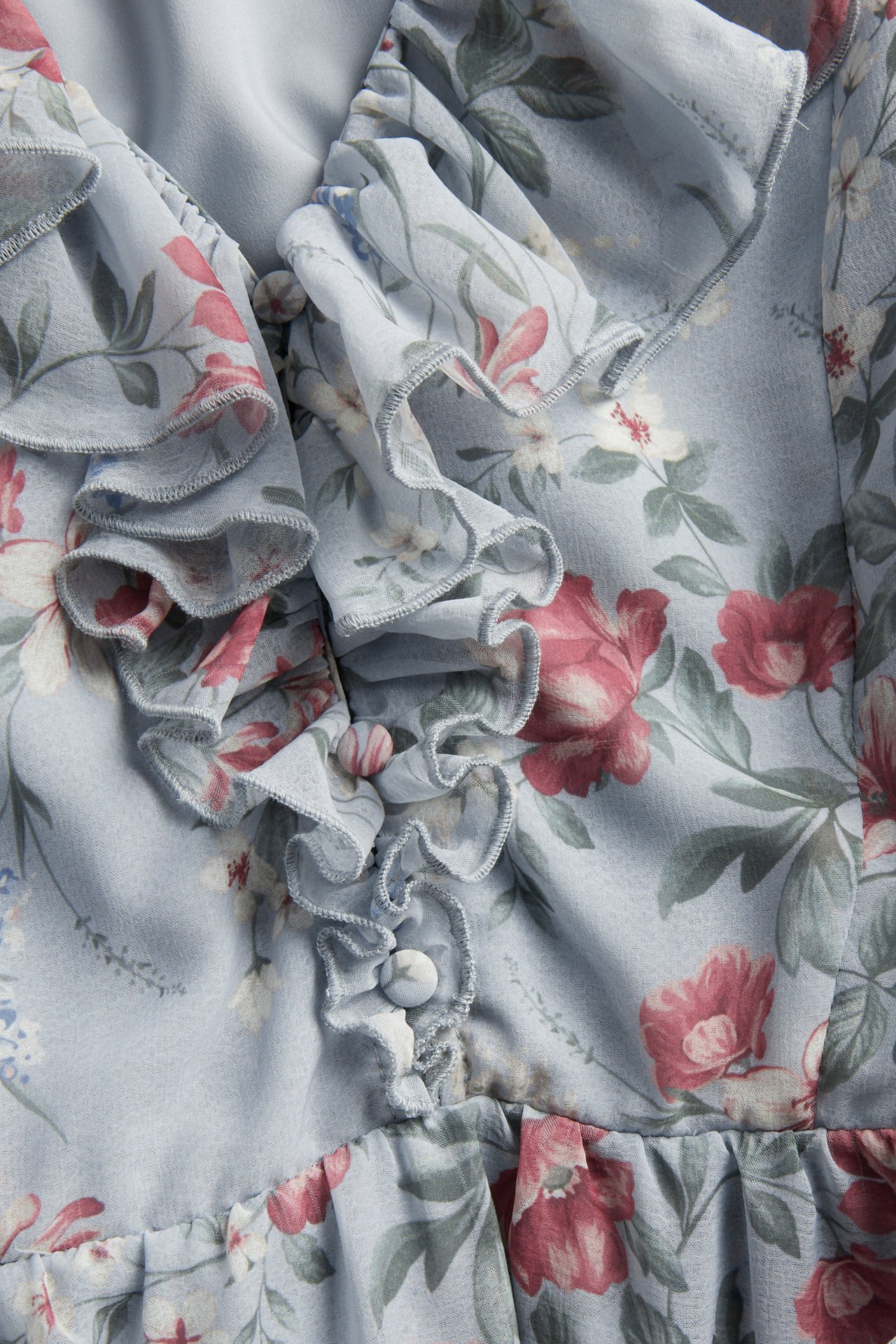 Close-up of a light blue floral chiffon dress featuring ruffles and covered buttons along the v-neck.