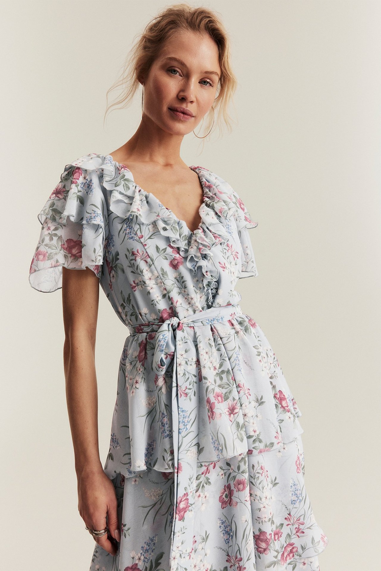 Vorderansicht: Frau in hellblauem geblümtem Chiffonkleid mit Rüschen, kurzen Ärmeln und Gürtel.