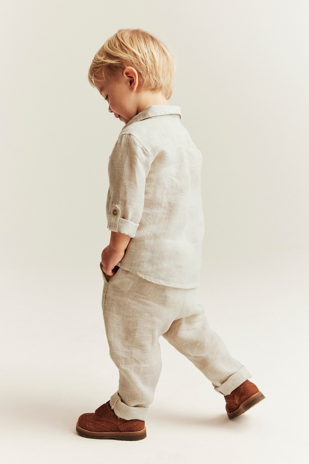 Side view of a baby boy wearing light beige linen drawstring trousers with rolled legs and a matching linen shirt.