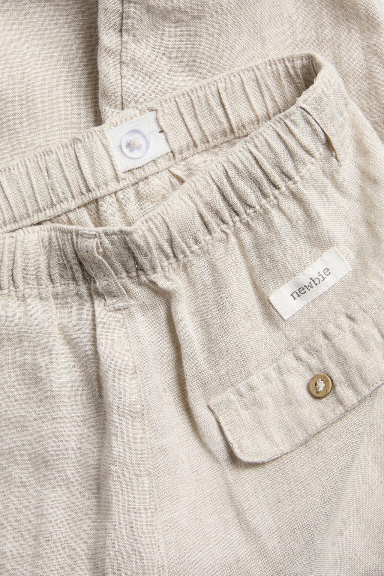 Close-up of light beige linen trousers with an elasticated waistband and a back pocket with a wooden button.