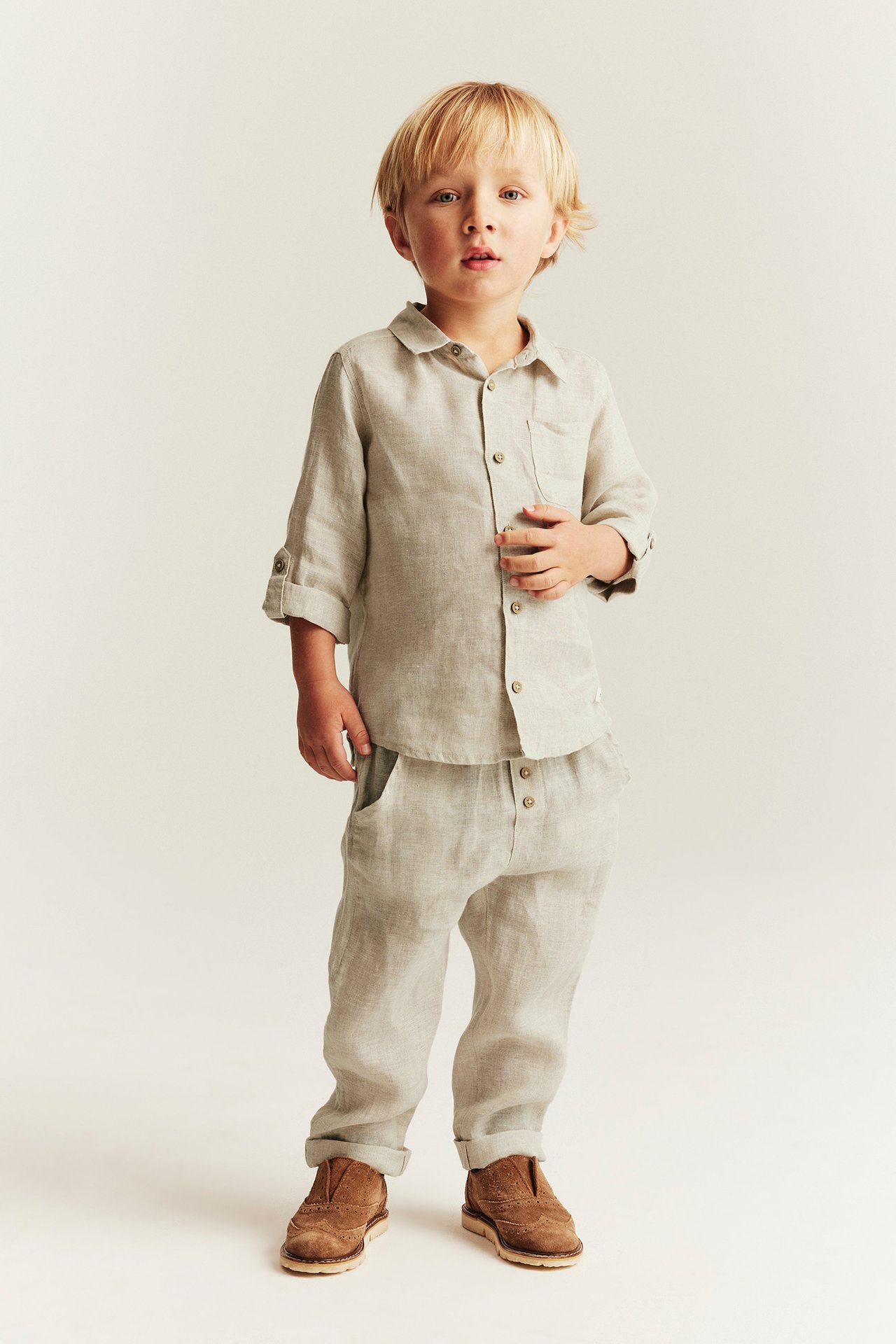 Vorderansicht eines Kindes in hellbeiger Leinenhose mit hochgekrempelten Beinen und passendem Leinenhemd.