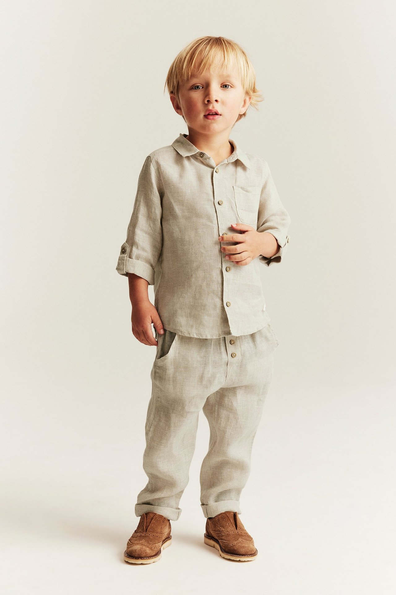 Vorderansicht eines Kindes in hellbeiger Leinenhose mit hochgekrempelten Beinen und passendem Leinenhemd.
