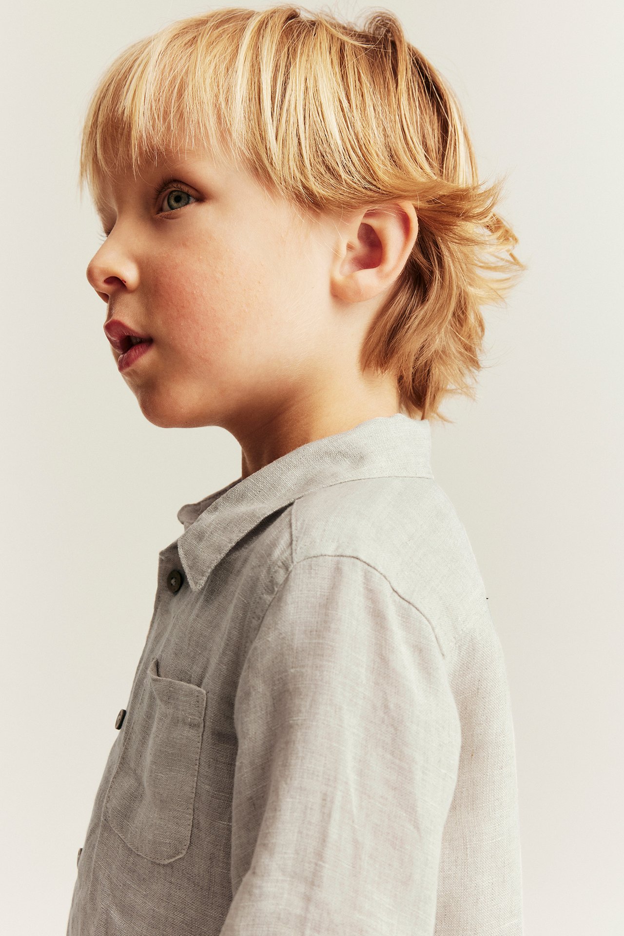 Side view of a kid wearing a light beige solid linen shirt with a collar and chest pocket.