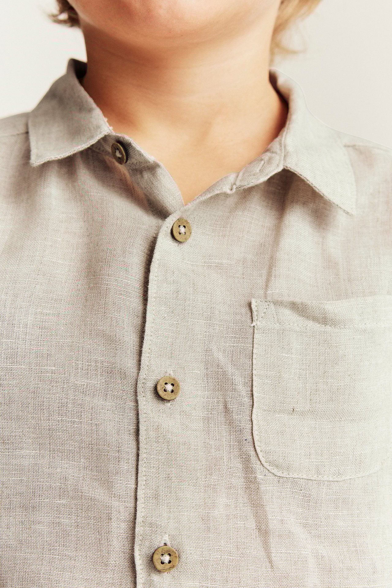 Close-up front view of a kid wearing a light beige linen shirt with a collar, buttons, and a chest pocket.