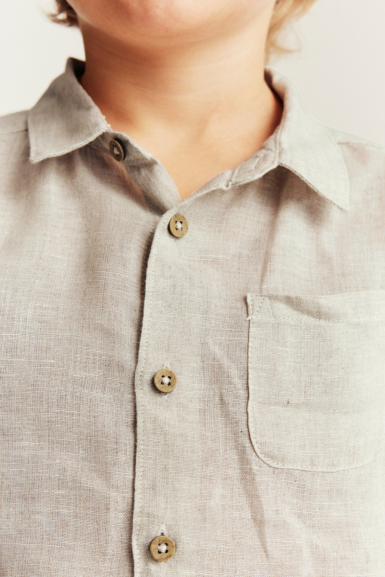 Close-up of a kid wearing a light beige linen collared shirt with button-front and chest pocket.