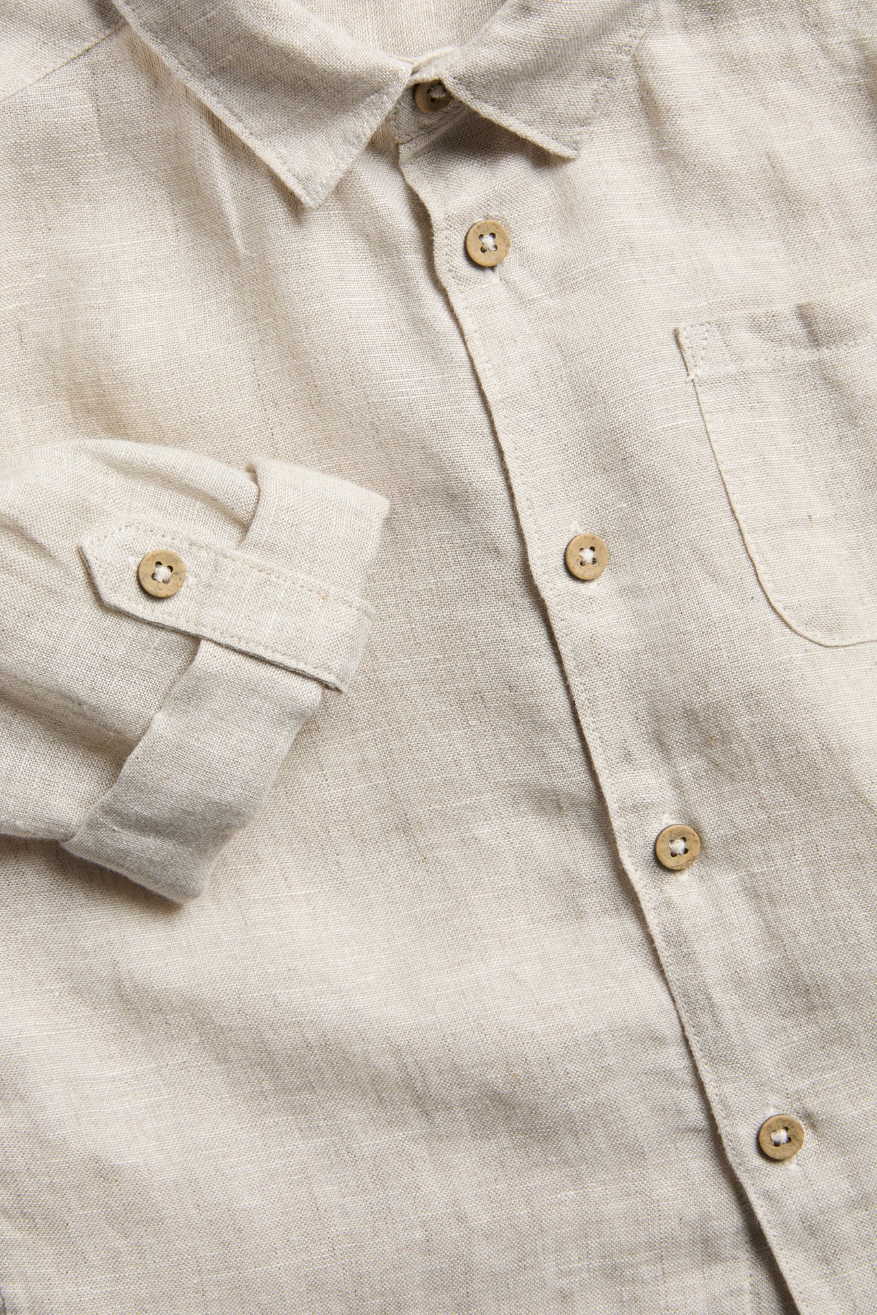 Close-up of a light beige linen shirt with collar, wooden buttons, rolled-up sleeve, and breast pocket.