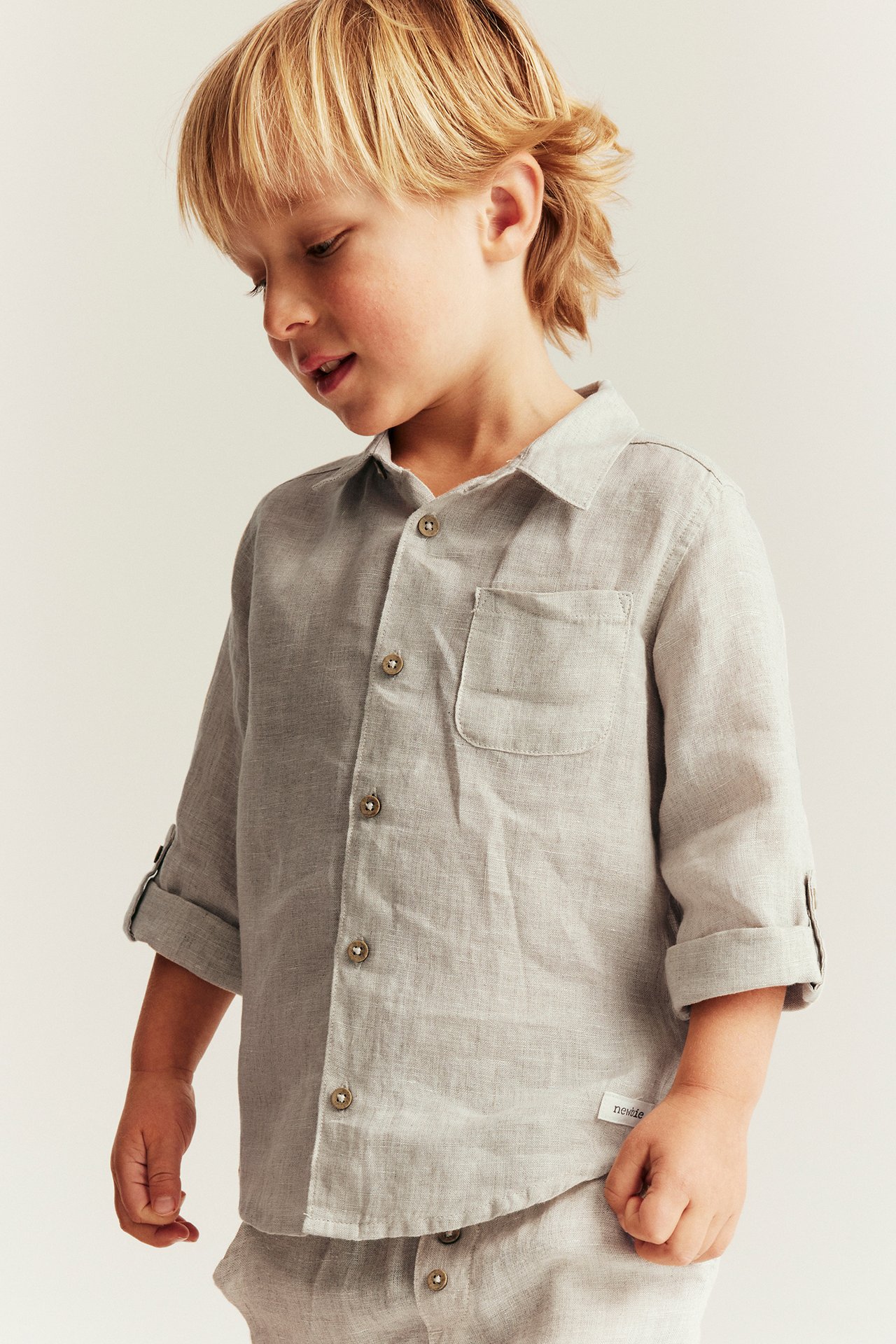 Close-up of a kid wearing a light beige linen shirt with rolled-up sleeves and matching linen bottoms.