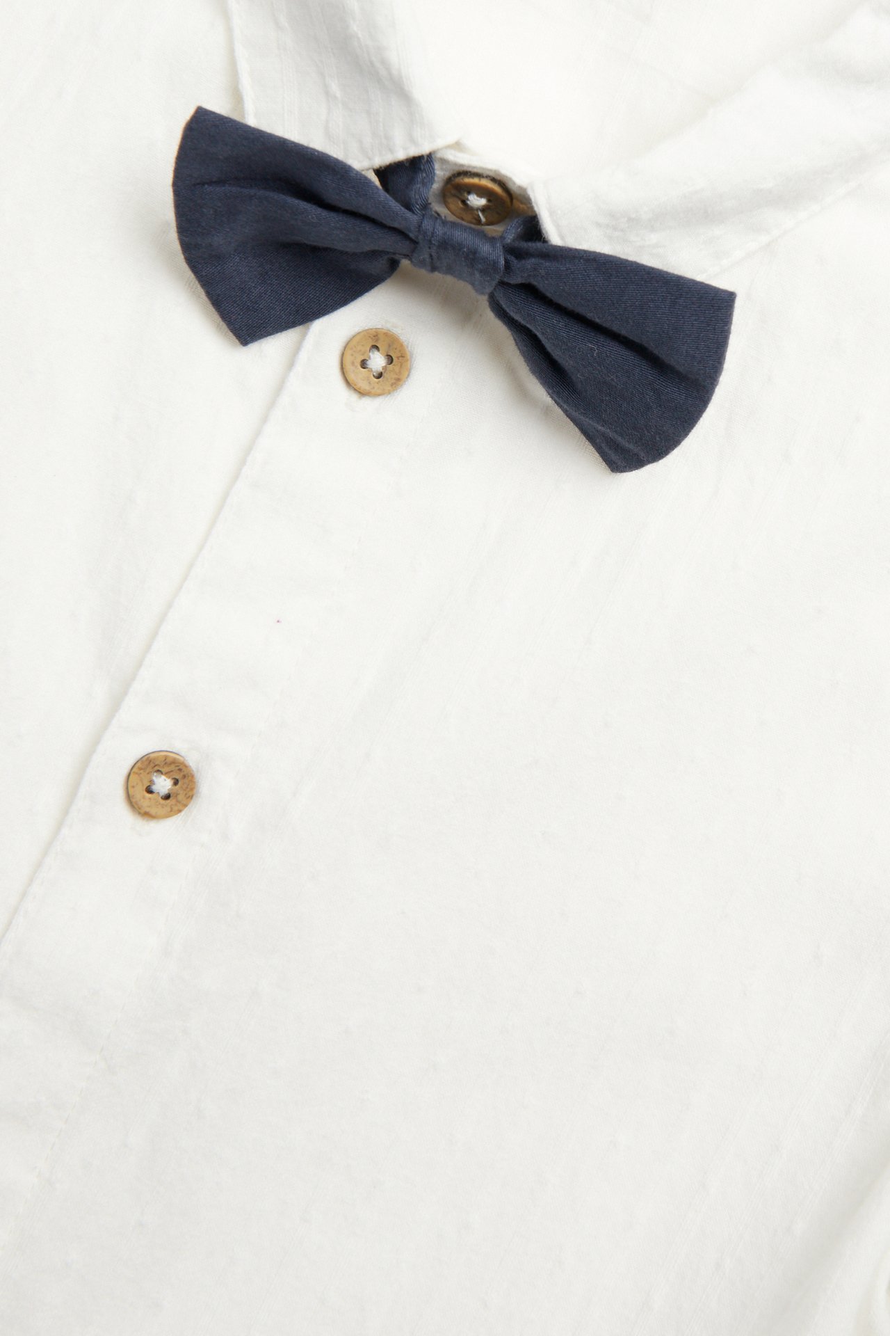 Close-up of an offwhite cotton shirt with collar, wooden buttons, and a dark blue bow tie.