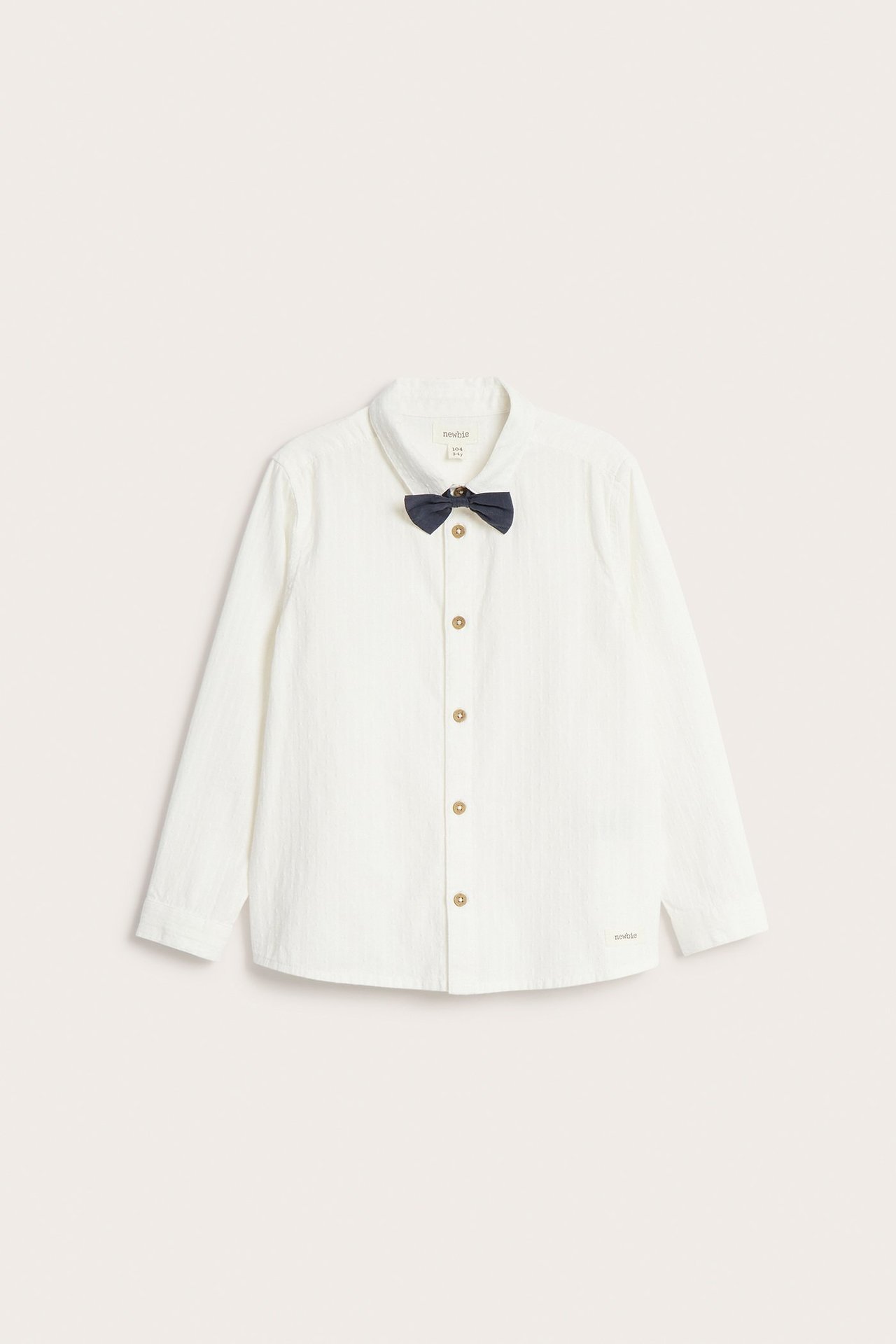 Front view of a kid's off-white cotton shirt with long sleeves, brown buttons, and a dark navy detachable bow tie.