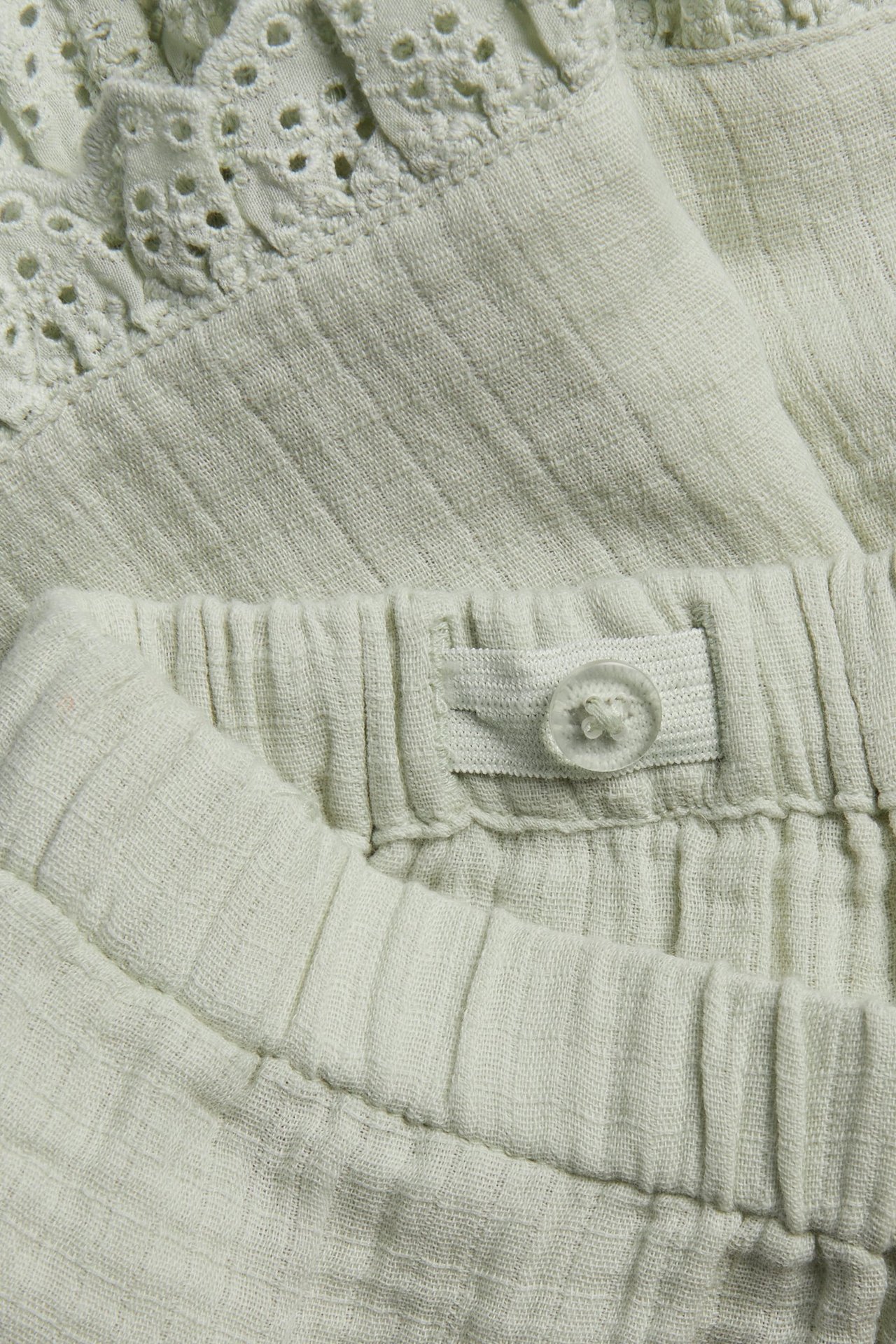 Nahaufnahme von hellgrünen gewebten Baumwollshorts mit Spitzenrüsche und verstellbarem Taillenknopf.