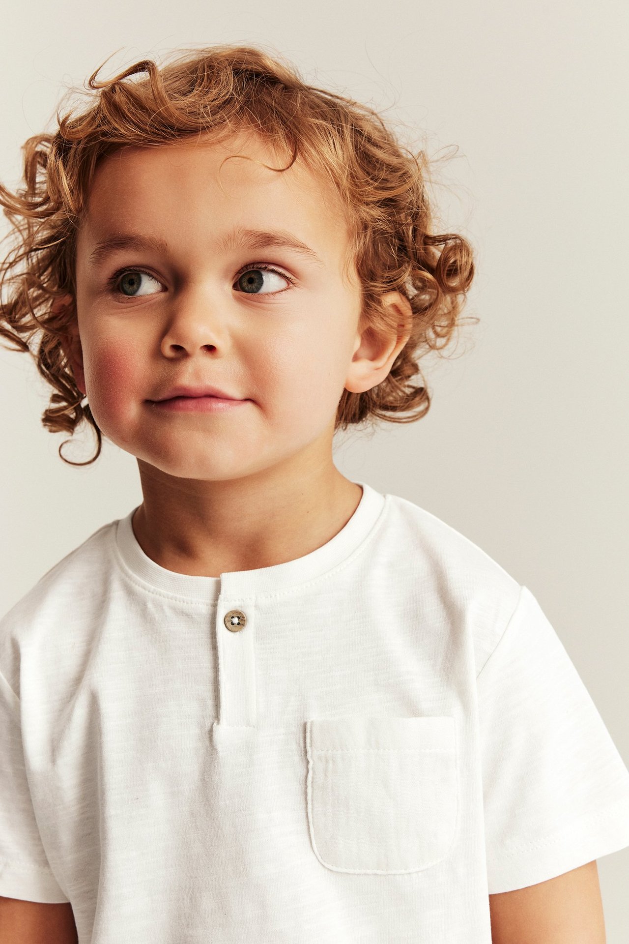 Close-up of a kid wearing an off-white slub jersey T-shirt with a single button and chest pocket.