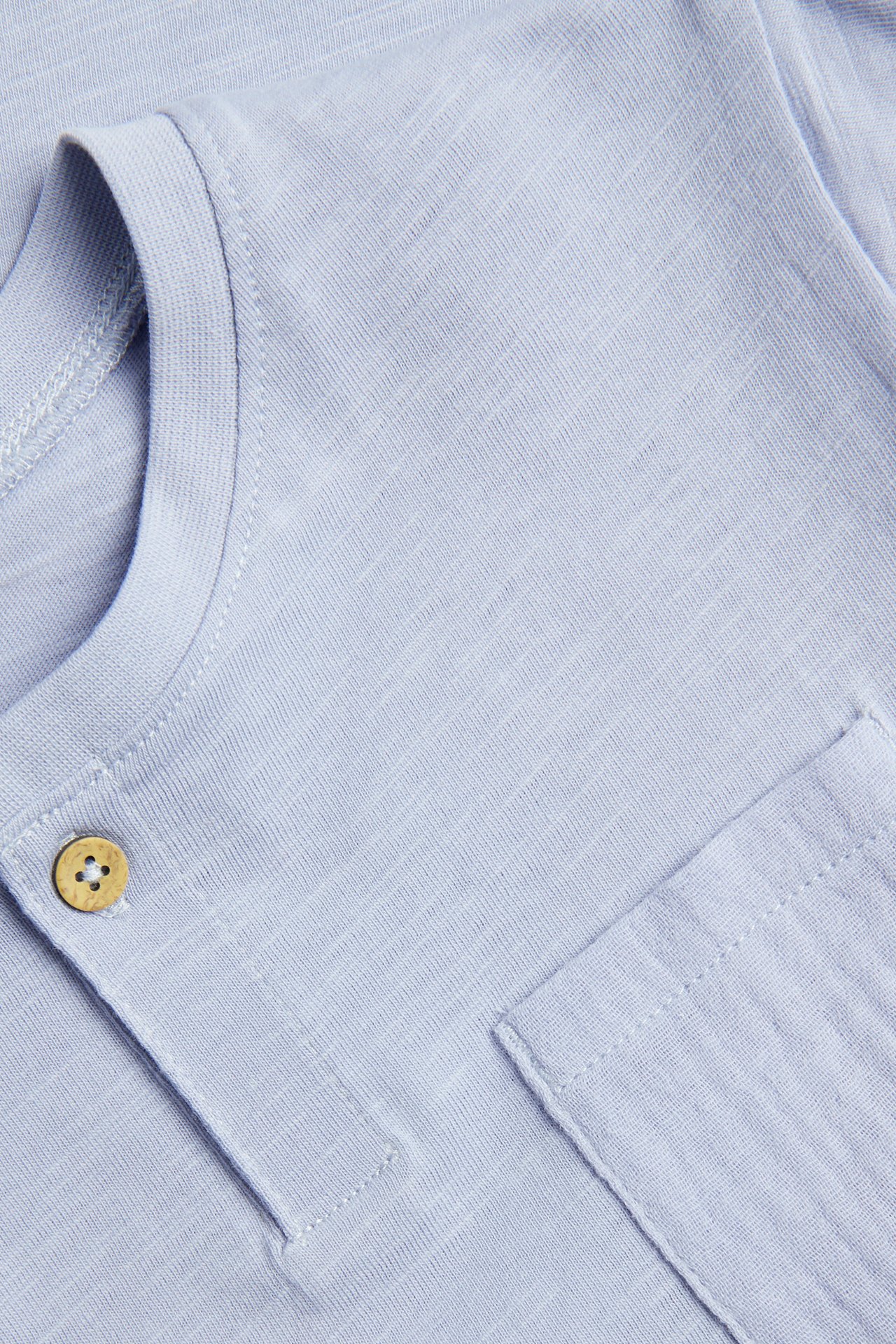 Close-up of a light blue slub jersey t-shirt with a woven chest pocket and one wooden button.