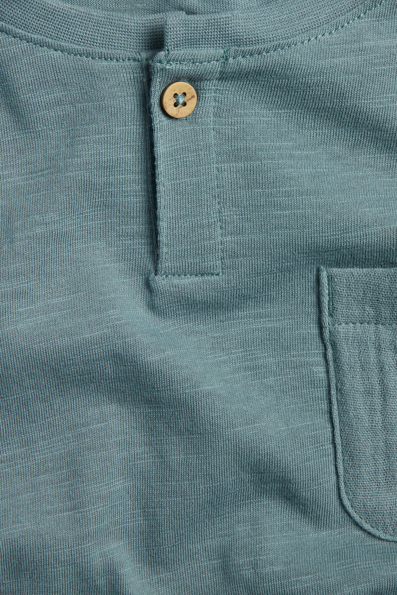 Close-up of a dark turquoise slub jersey T-shirt with a wooden button and a chest pocket.