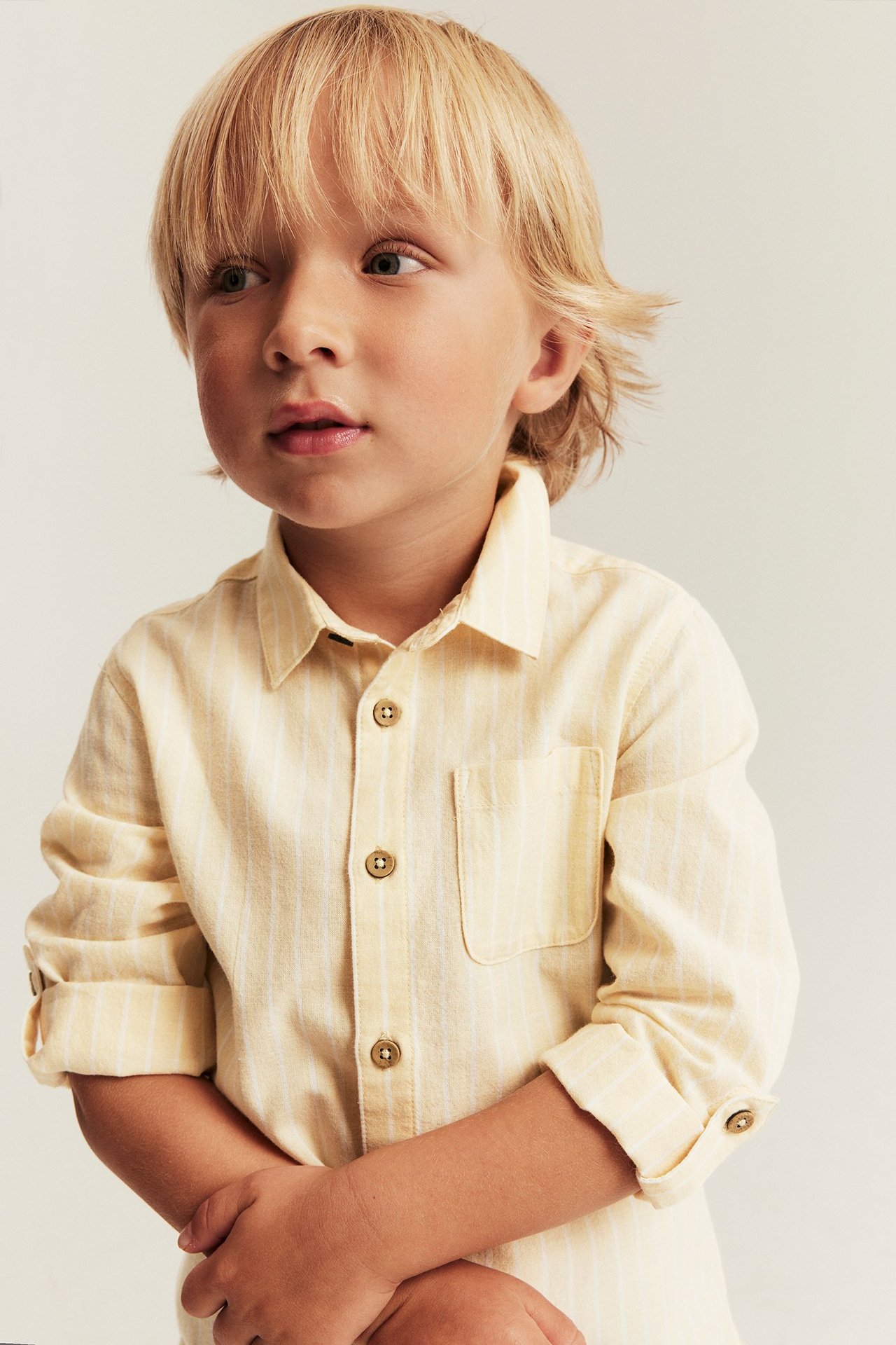Front view: Kid wearing a yellow striped shirt with collar, button front, chest pocket, and rolled sleeves.