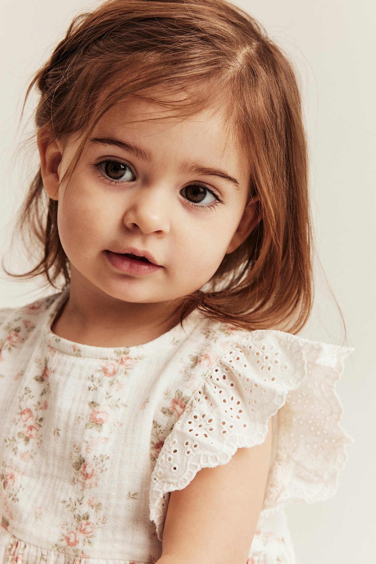 Nahaufnahme von vorne eines Kindes in einem cremeweißen geblümten Musselin-Top mit bestickten Rüschenärmeln.