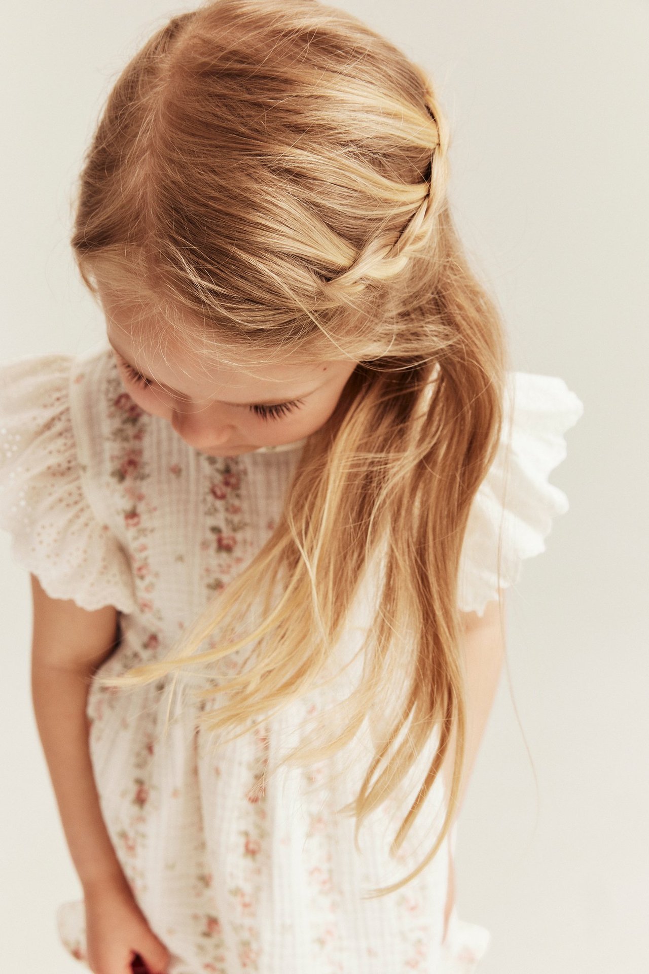 Nahaufnahme eines Kindes in einem cremeweißen geblümten Musselin-Top mit bestickten Rüschenärmeln, von oben.