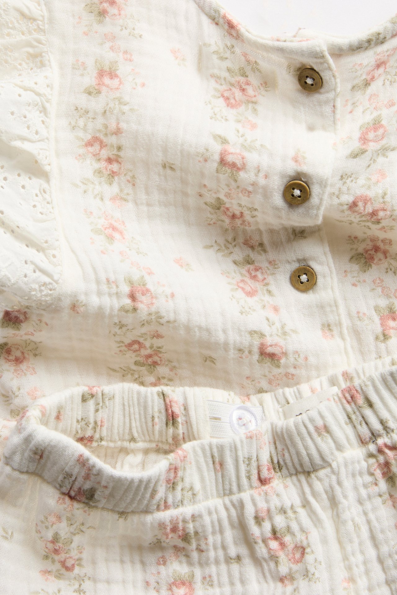 Nahaufnahme eines offwhite geblümten Musselin-Kinder-Sets: Peplum-Oberteil mit Rüschenärmeln und Shorts.