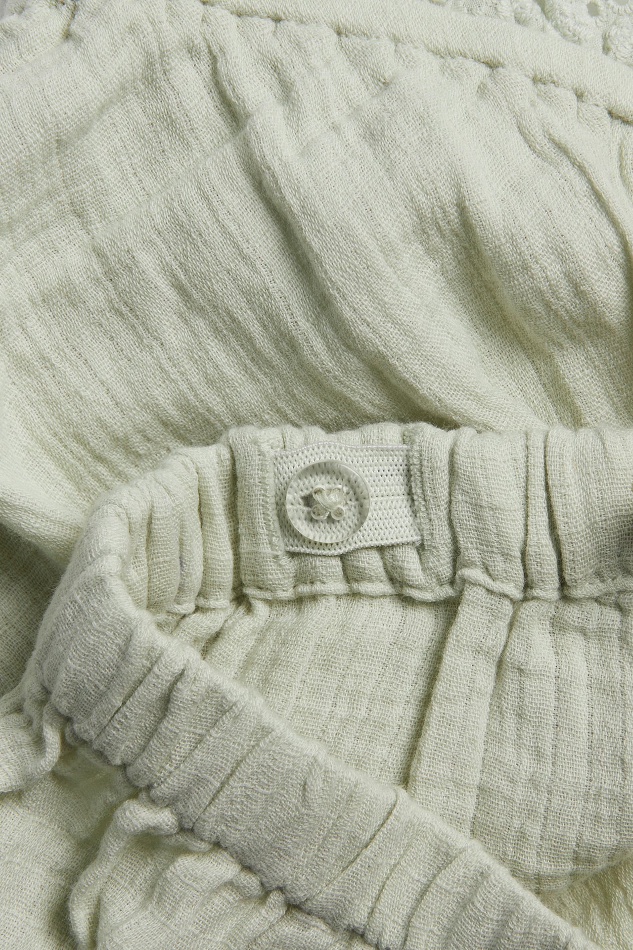 Close-up of light green cotton shorts with adjustable elastic waistband and a lace flounce.