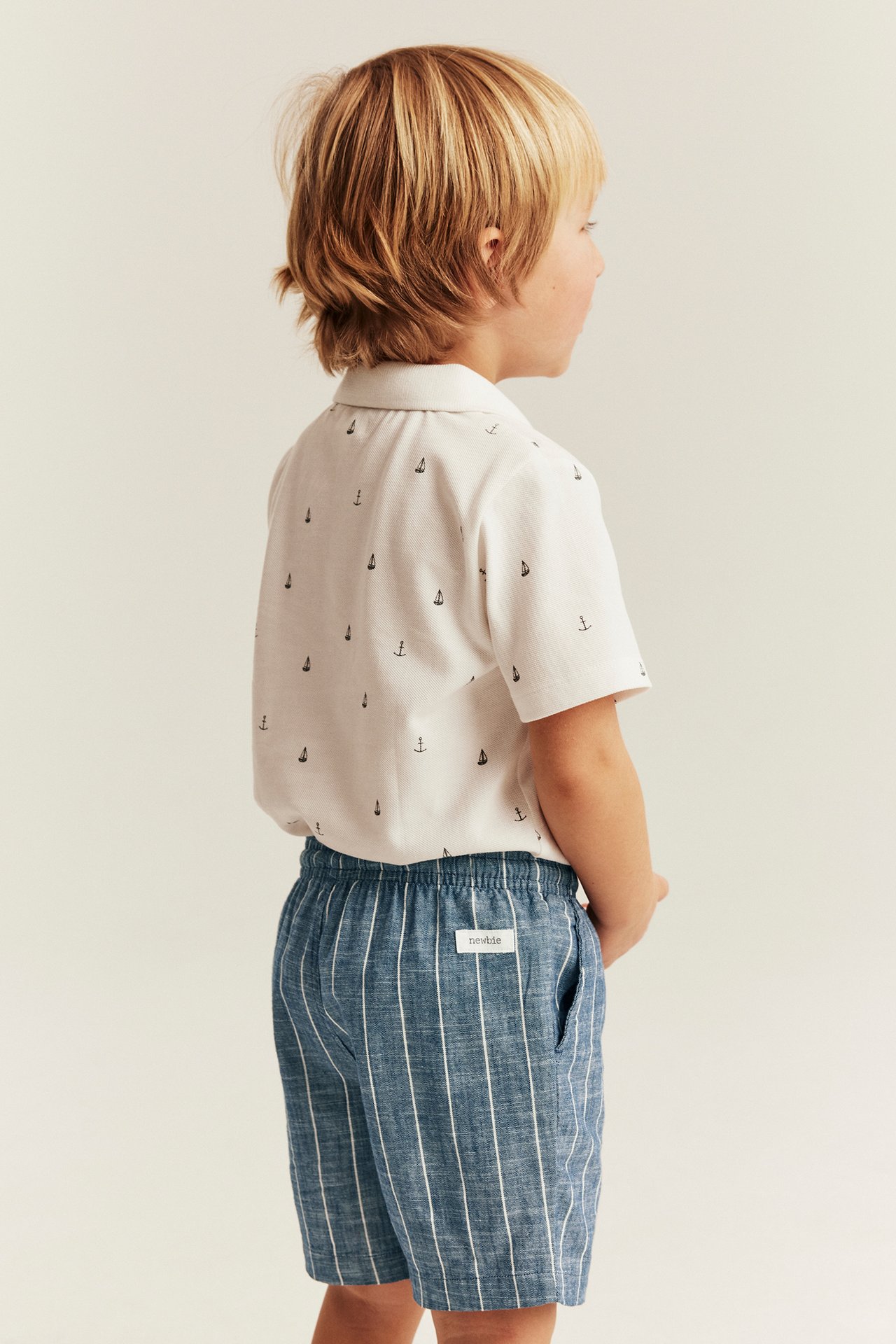 Seitenansicht eines Kindes in blauen gestreiften Webshorts mit Gummizug und weißem Hemd.