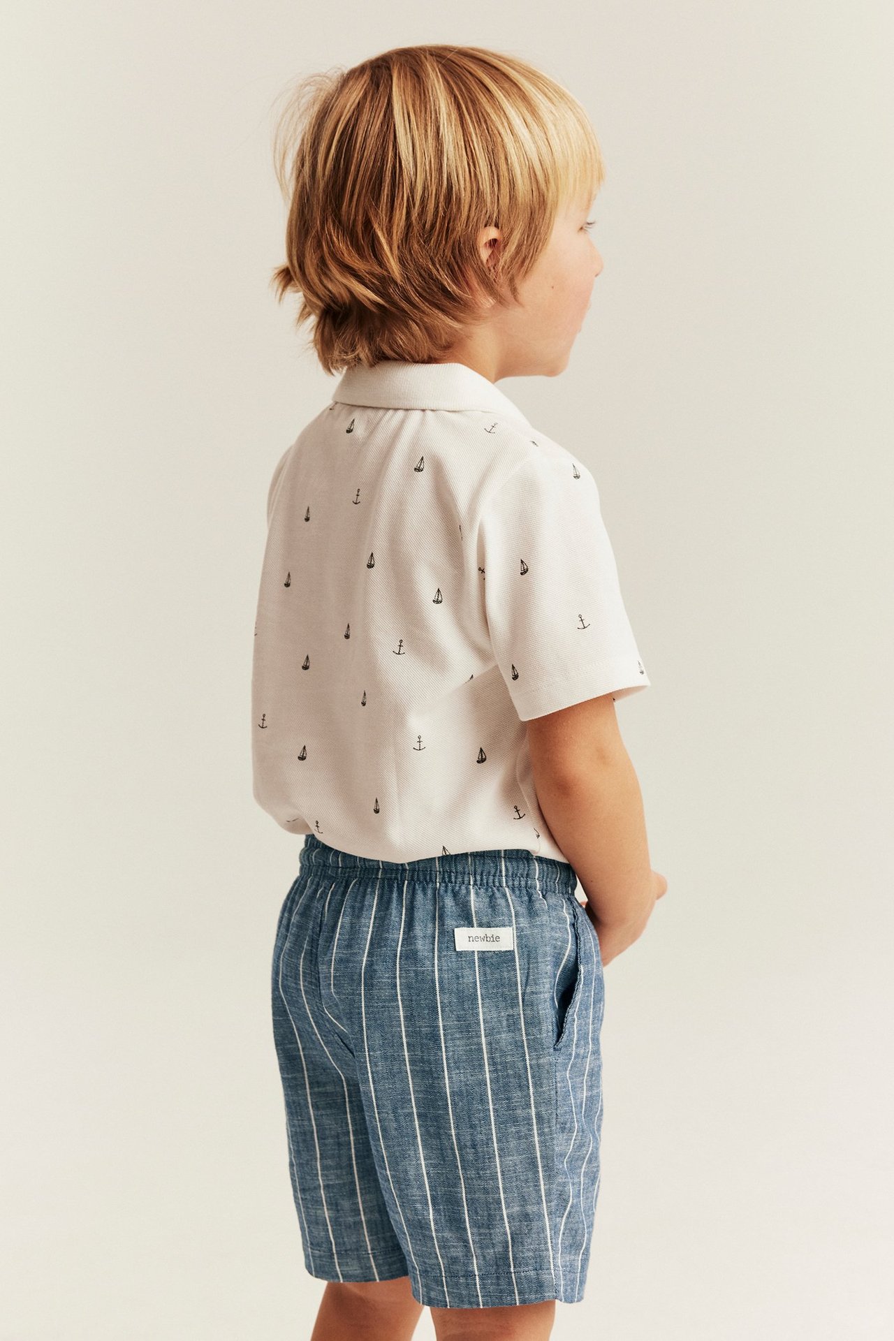 Seitenansicht eines Kindes in blauen gestreiften Webshorts mit Gummizug und weißem Hemd.