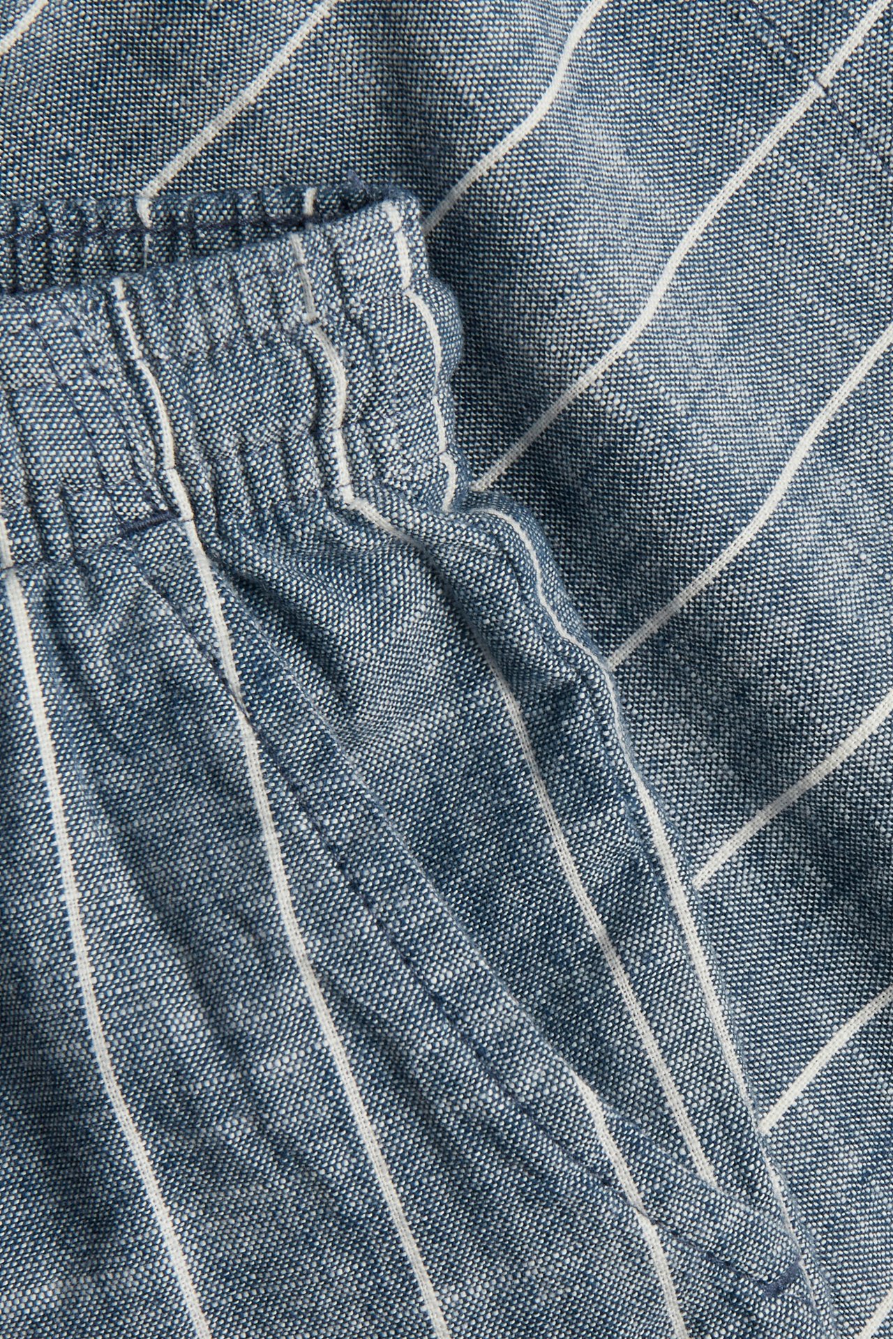 Nahaufnahme von blau-weiß gestreiften, gewebten Baumwollshorts mit elastischem Bund und Seitentasche.