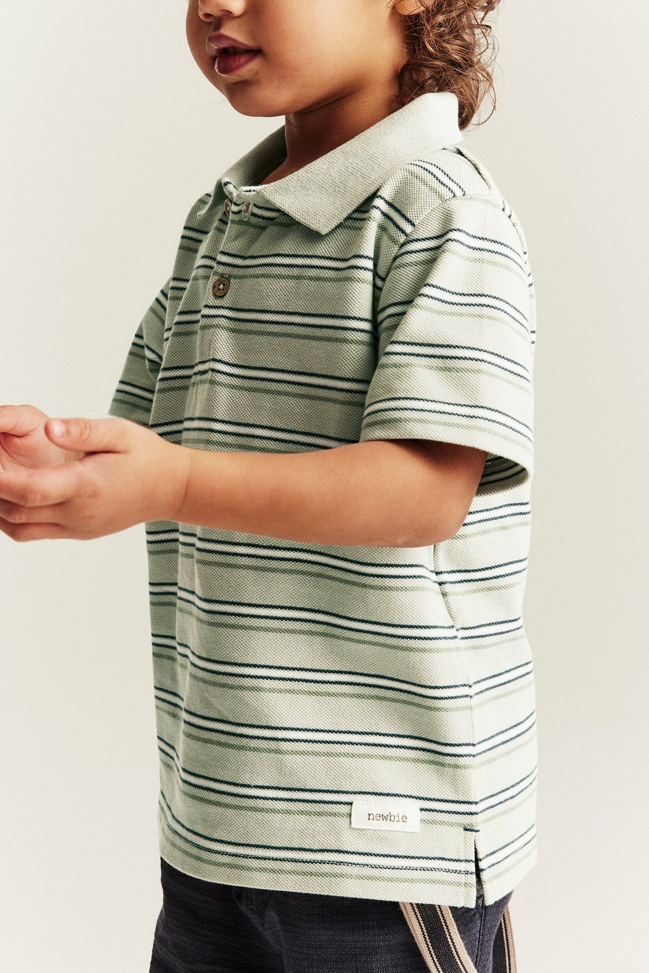 Side-front view of a kid in a green striped cotton short-sleeved polo shirt with buttons.