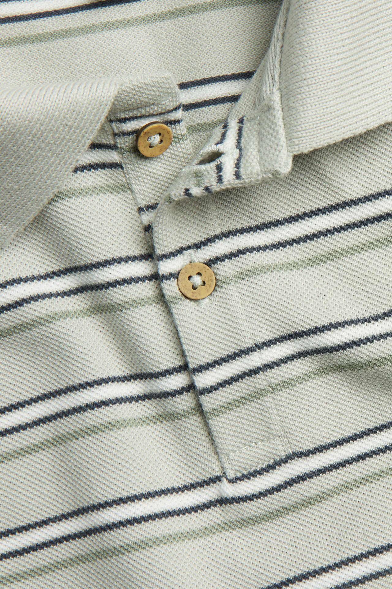 Close-up of a light green striped short-sleeved polo shirt with a collar and two wooden buttons.