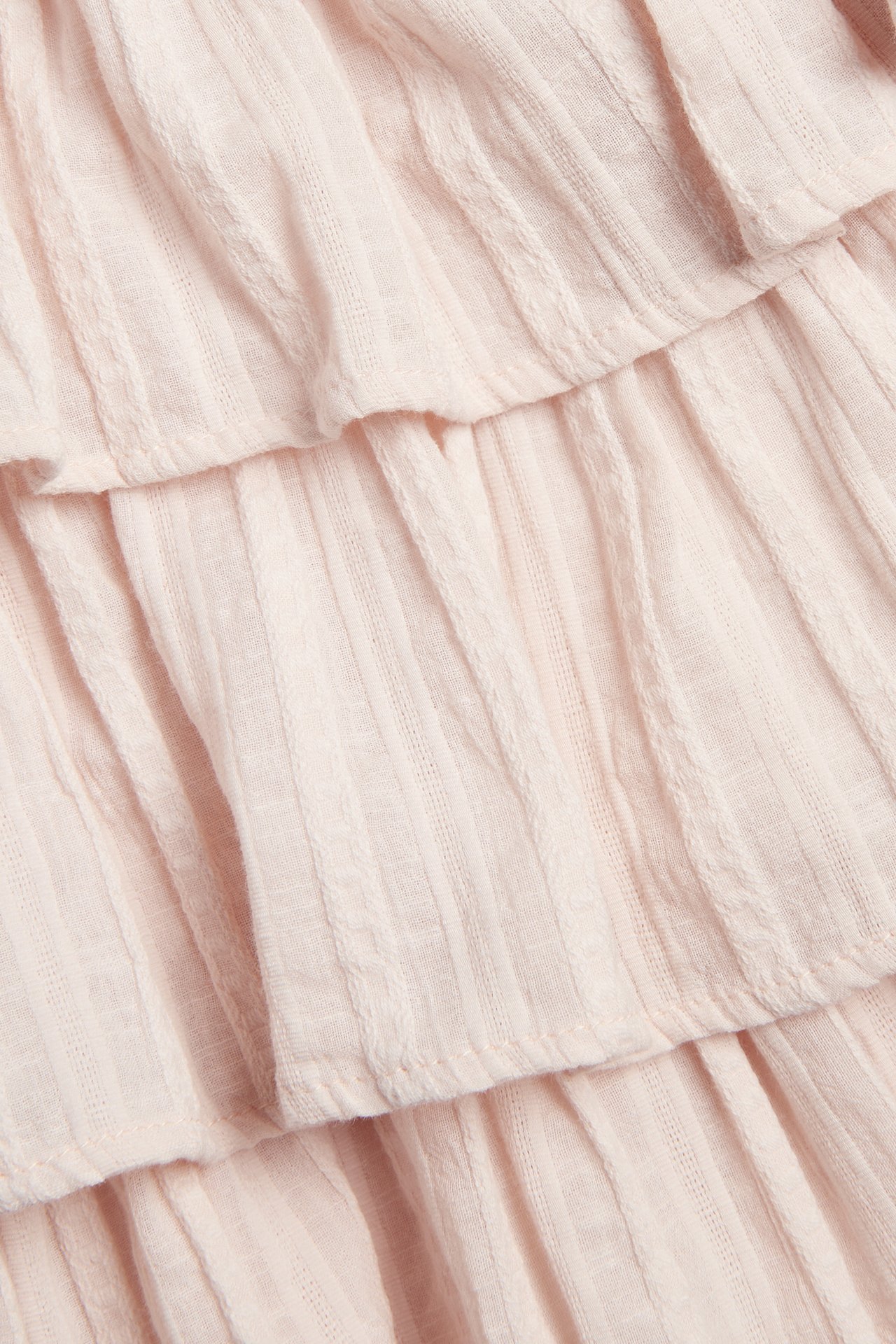 Close-up of a light pink woven blouse featuring ruffled tiers and a structured stripe pattern.