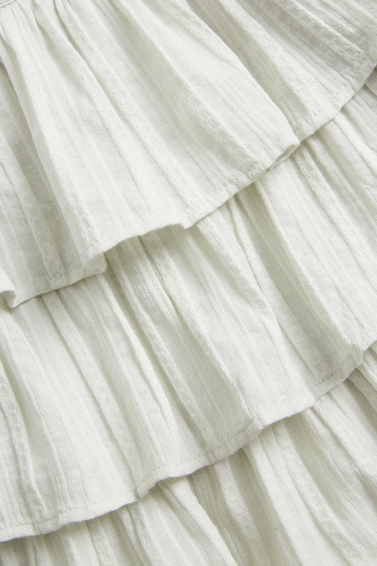 Close-up of a light green woven cotton blouse featuring textured stripes and ruffles.