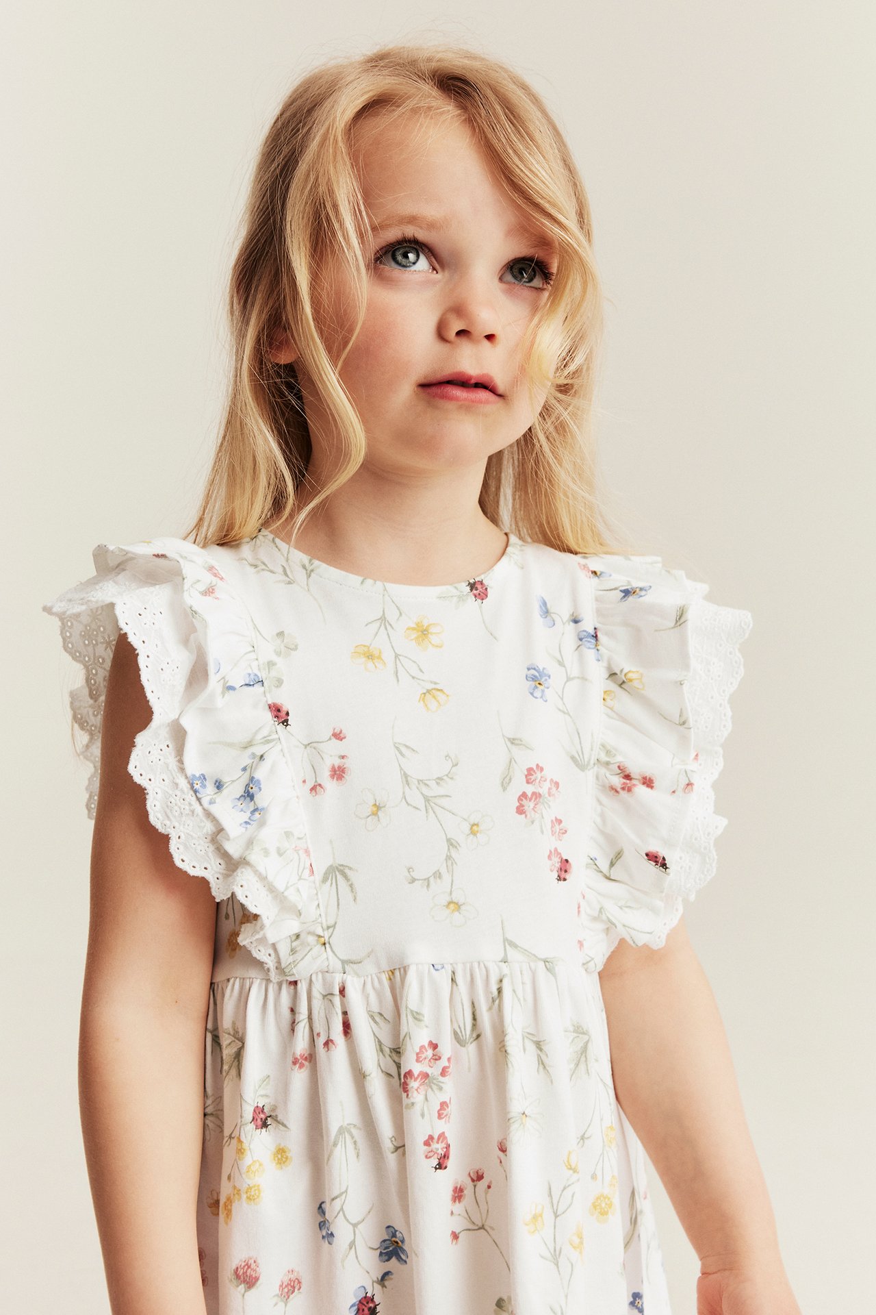 Nahaufnahme, Vorderansicht eines Kindes im off-weißen Blumen-Jerseykleid mit Rüschen und Spitzendetails.