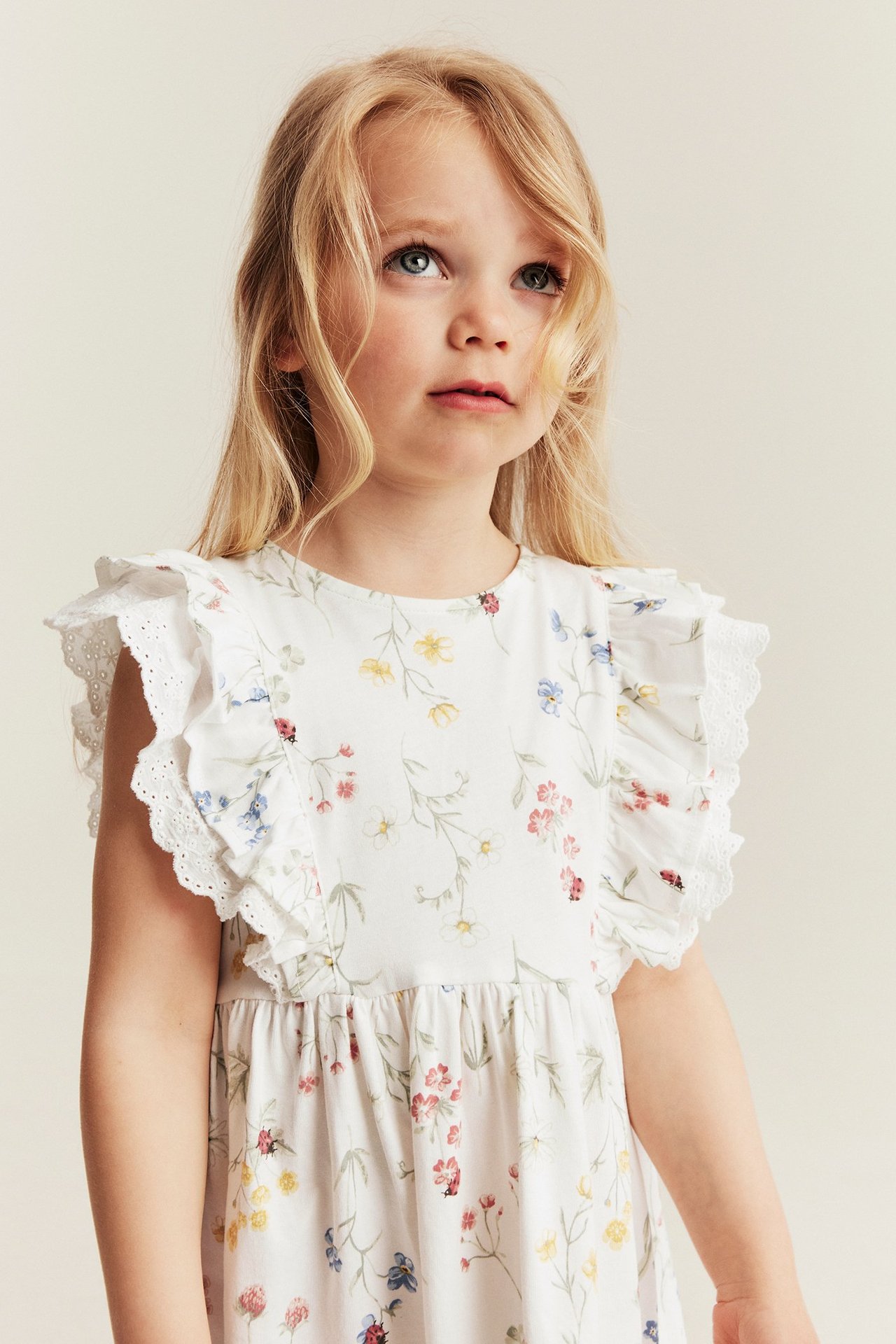 Nahaufnahme, Vorderansicht eines Kindes im off-weißen Blumen-Jerseykleid mit Rüschen und Spitzendetails.