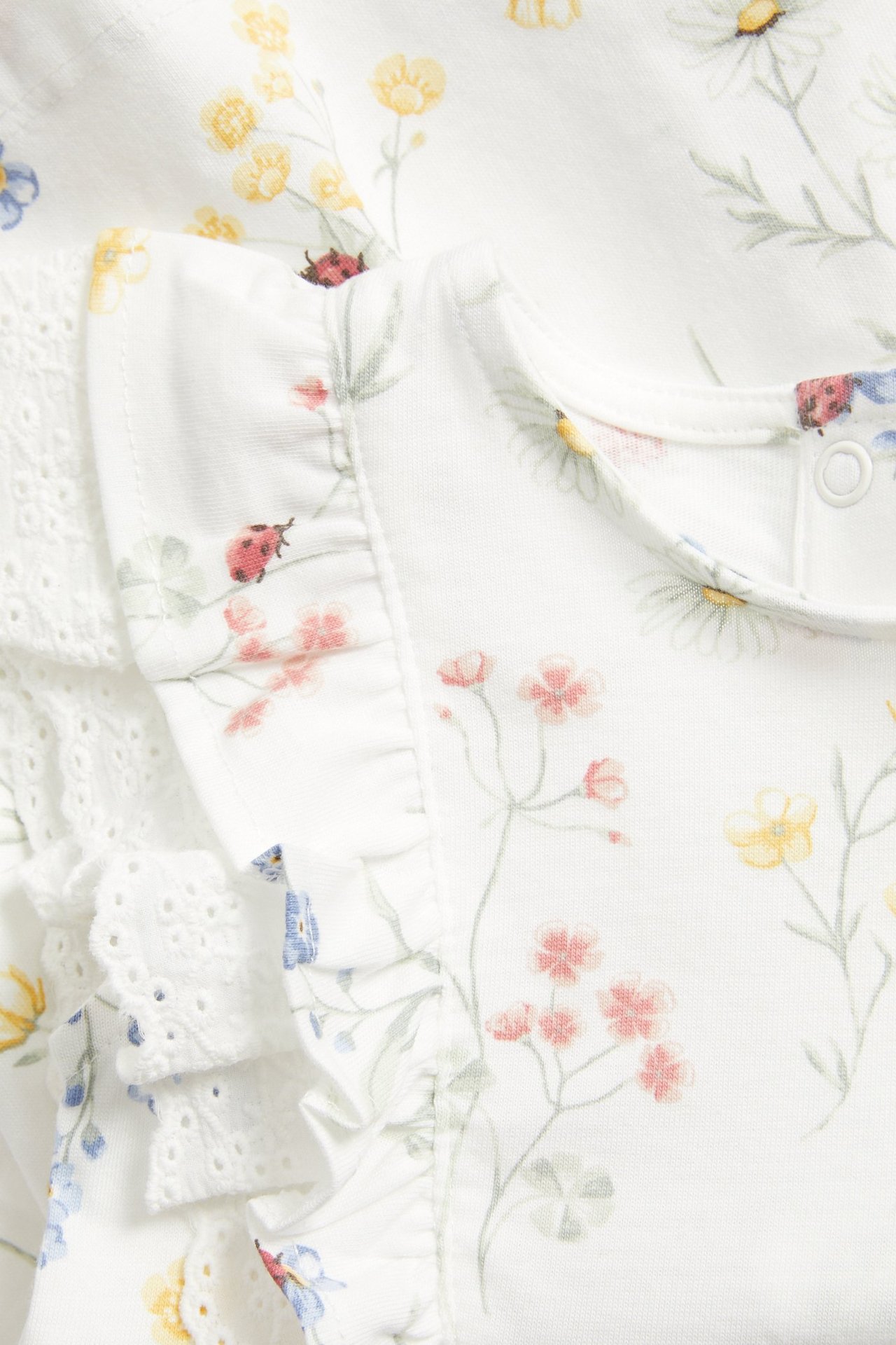 Nahaufnahme, Vorderansicht, eines off-white Baumwoll-Jerseykleides mit Blumenmuster, Rüschen und Spitzendetails.