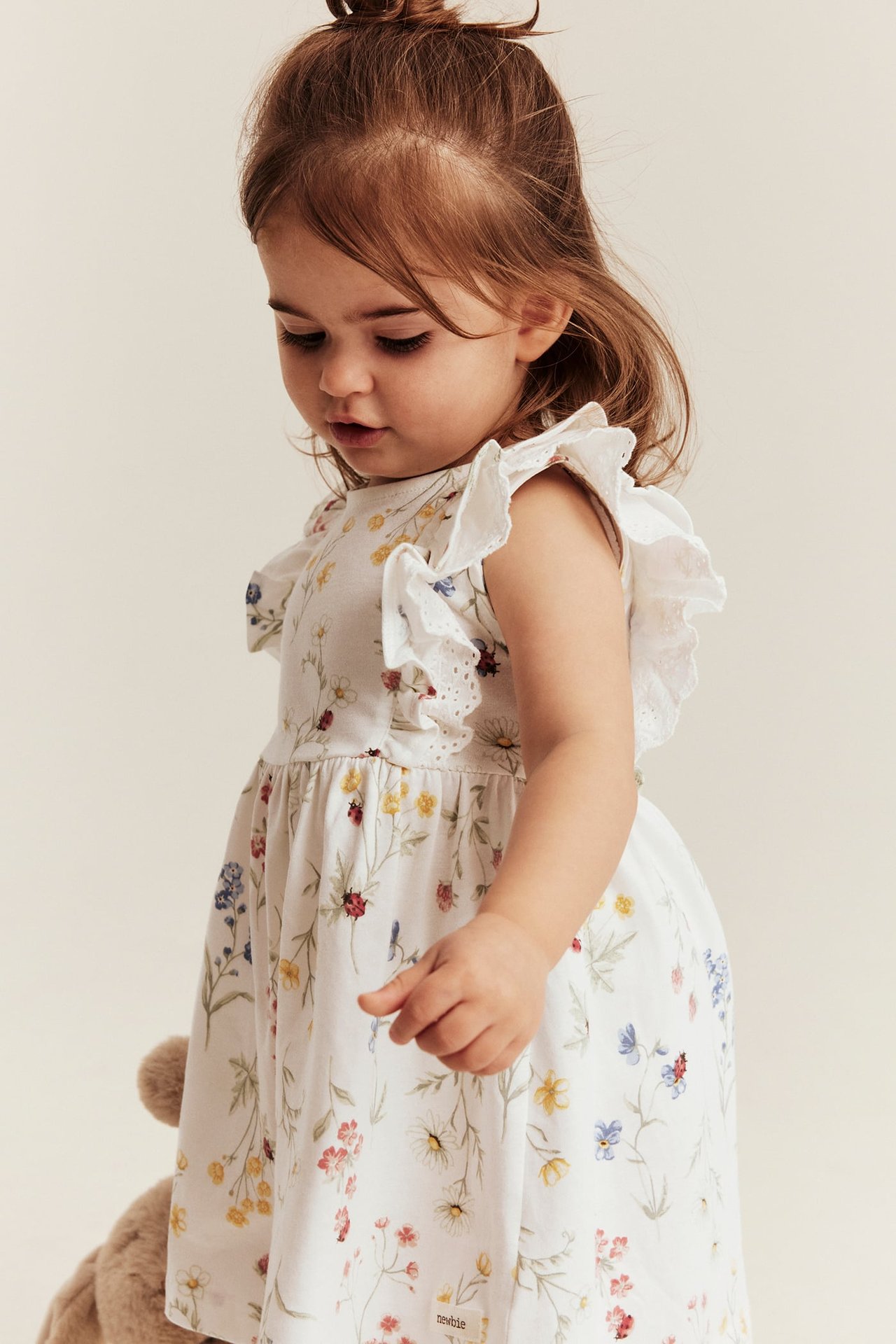 Seitenansicht eines Babys in einem cremeweißen geblümten Jerseykleid mit Rüschen und Spitze an den Ärmeln.