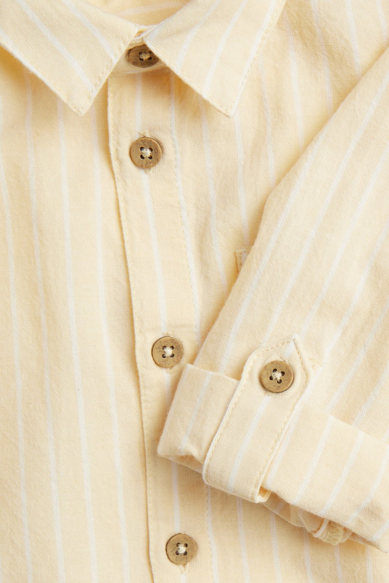 Close-up: yellow striped woven cotton shirt with collar, button-front, and rolled-up sleeves with buttons.