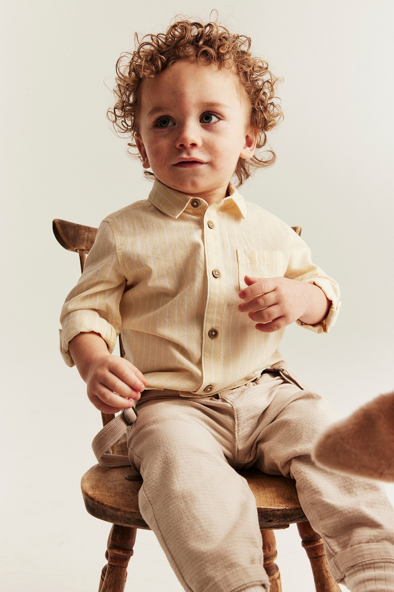 Front view: Baby in a yellow striped cotton shirt with collar, buttons, rolled sleeves, and beige trousers.