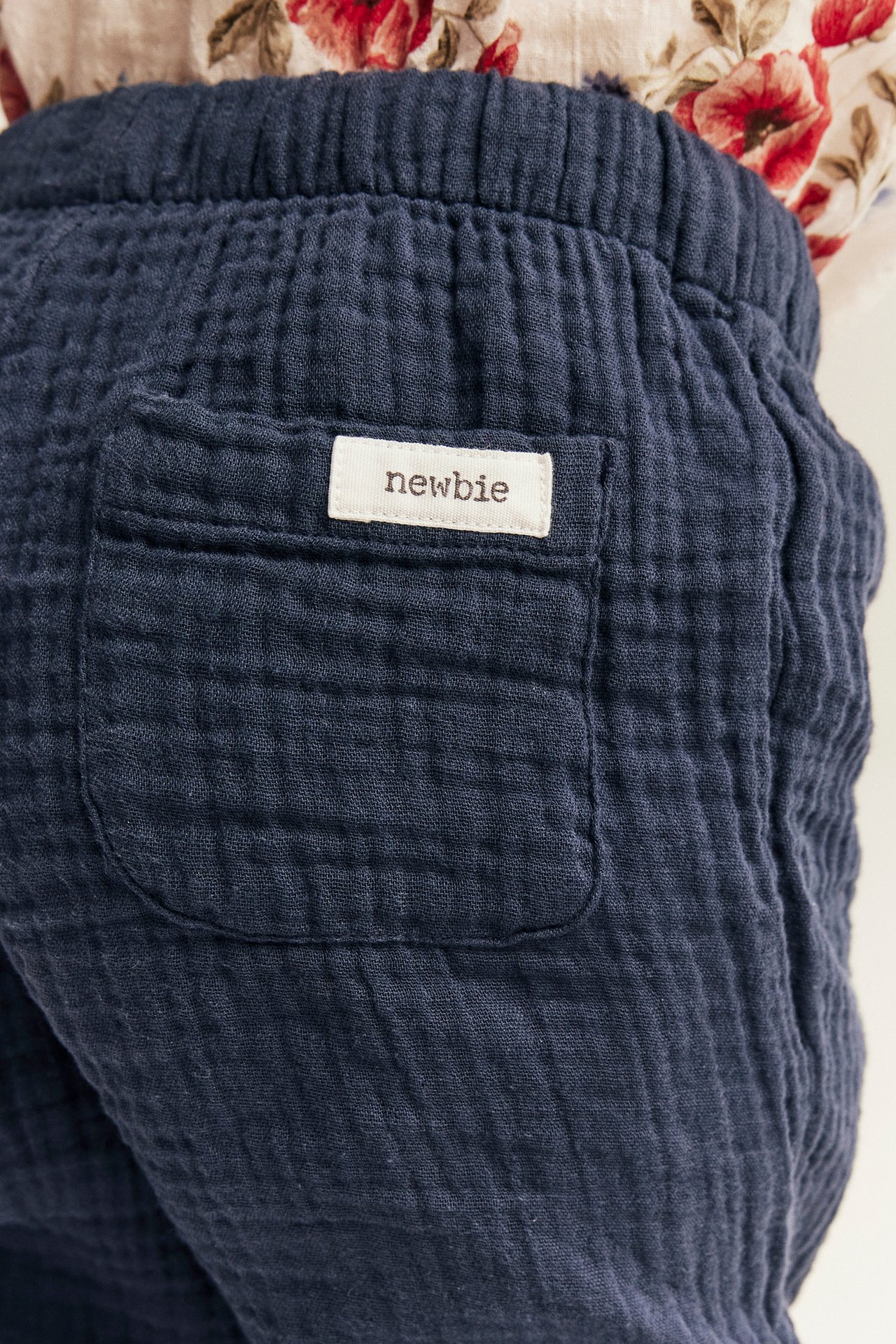 Close-up back view: kid's dark blue muslin trousers with elastic waist and a back pocket, worn with a floral top.
