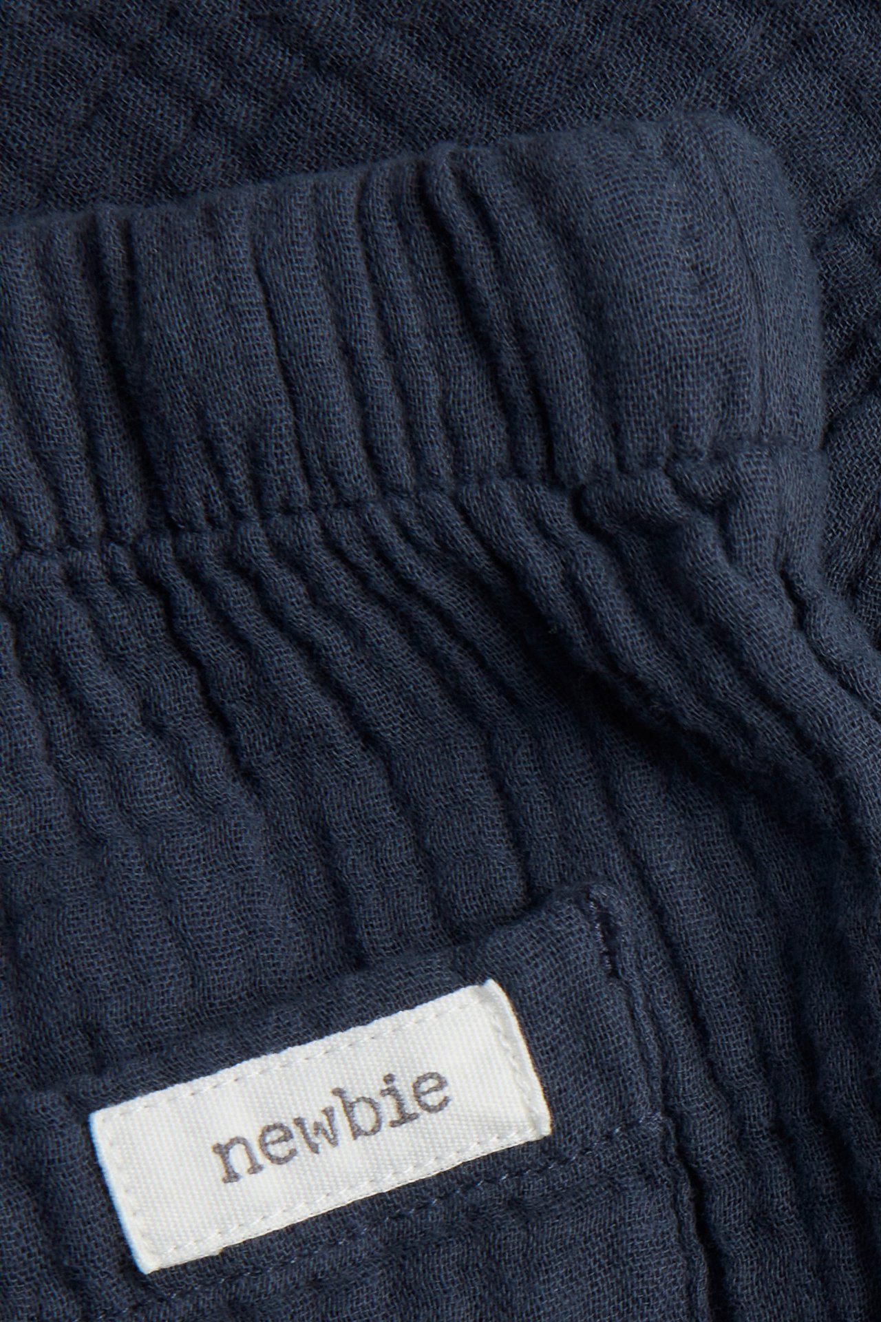 Close-up of dark blue cotton muslin trousers with elastic waistband and 'newbie' label on back pocket.