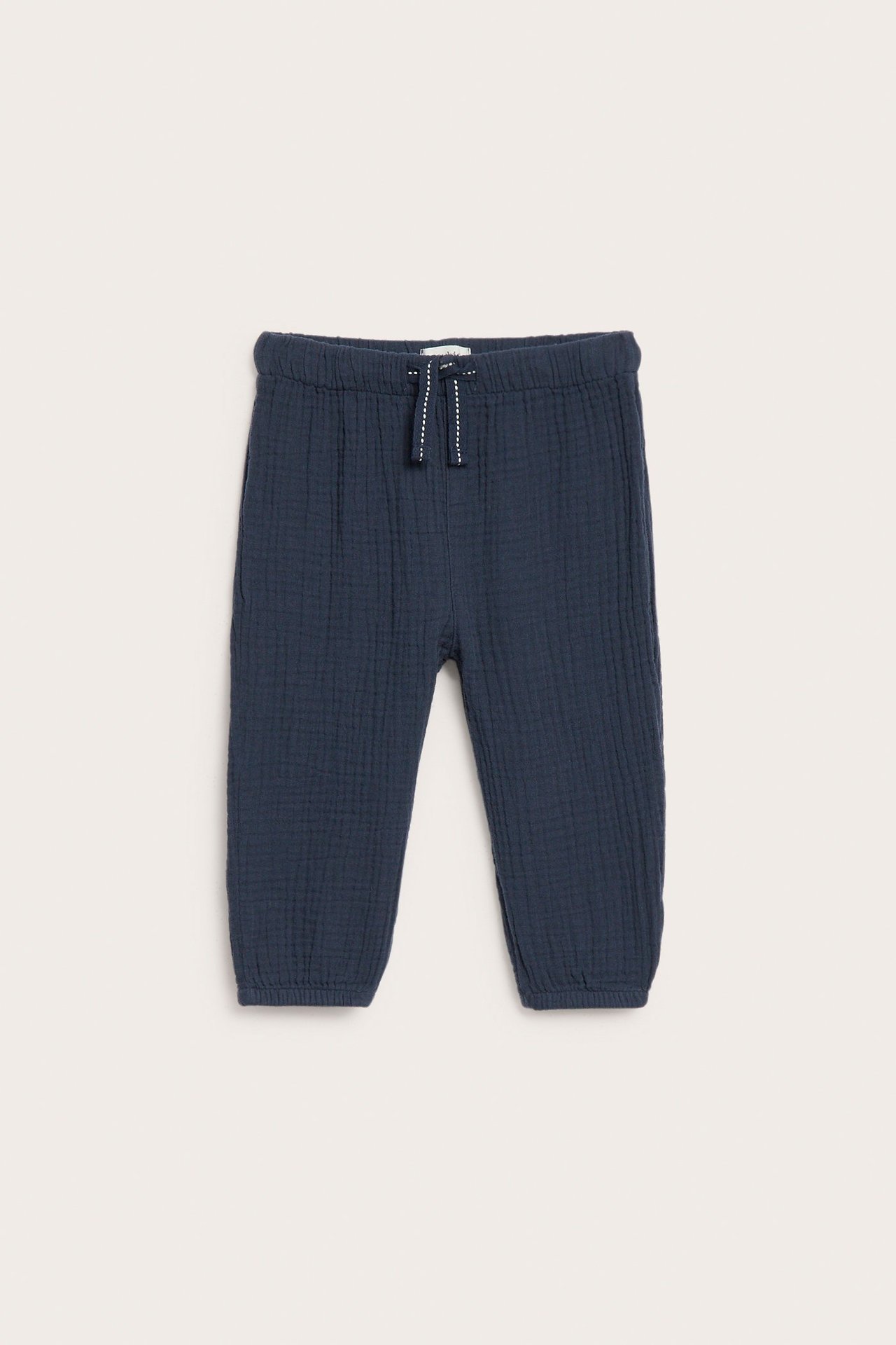 Vorderansicht einer dunkelblauen Kinderhose aus Baumwollmusselin mit Gummizugbund, weißem Kordelzug und Bündchen.