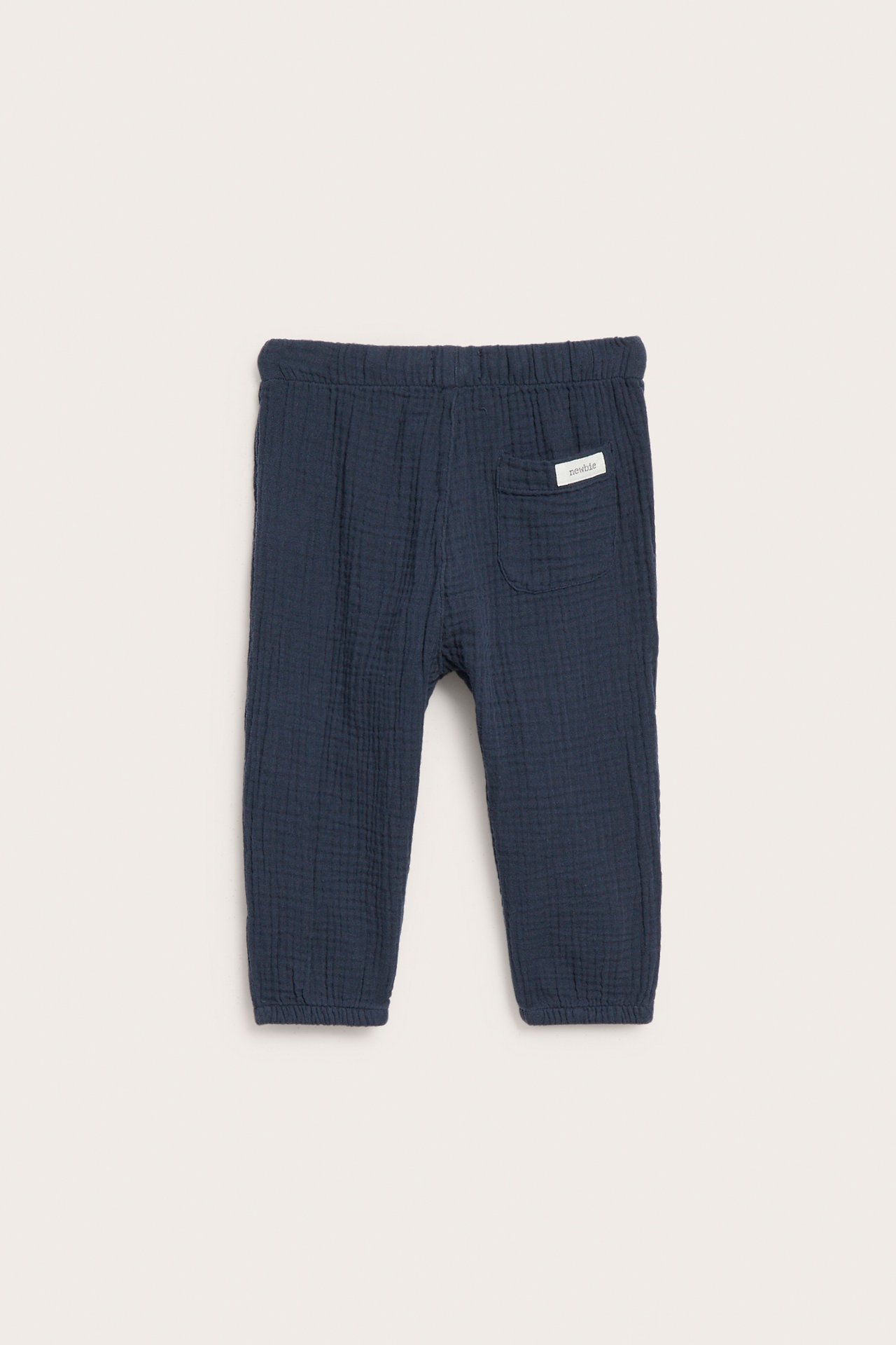 Back view of dark blue cotton muslin baby pants with an elastic waist and a back patch pocket.