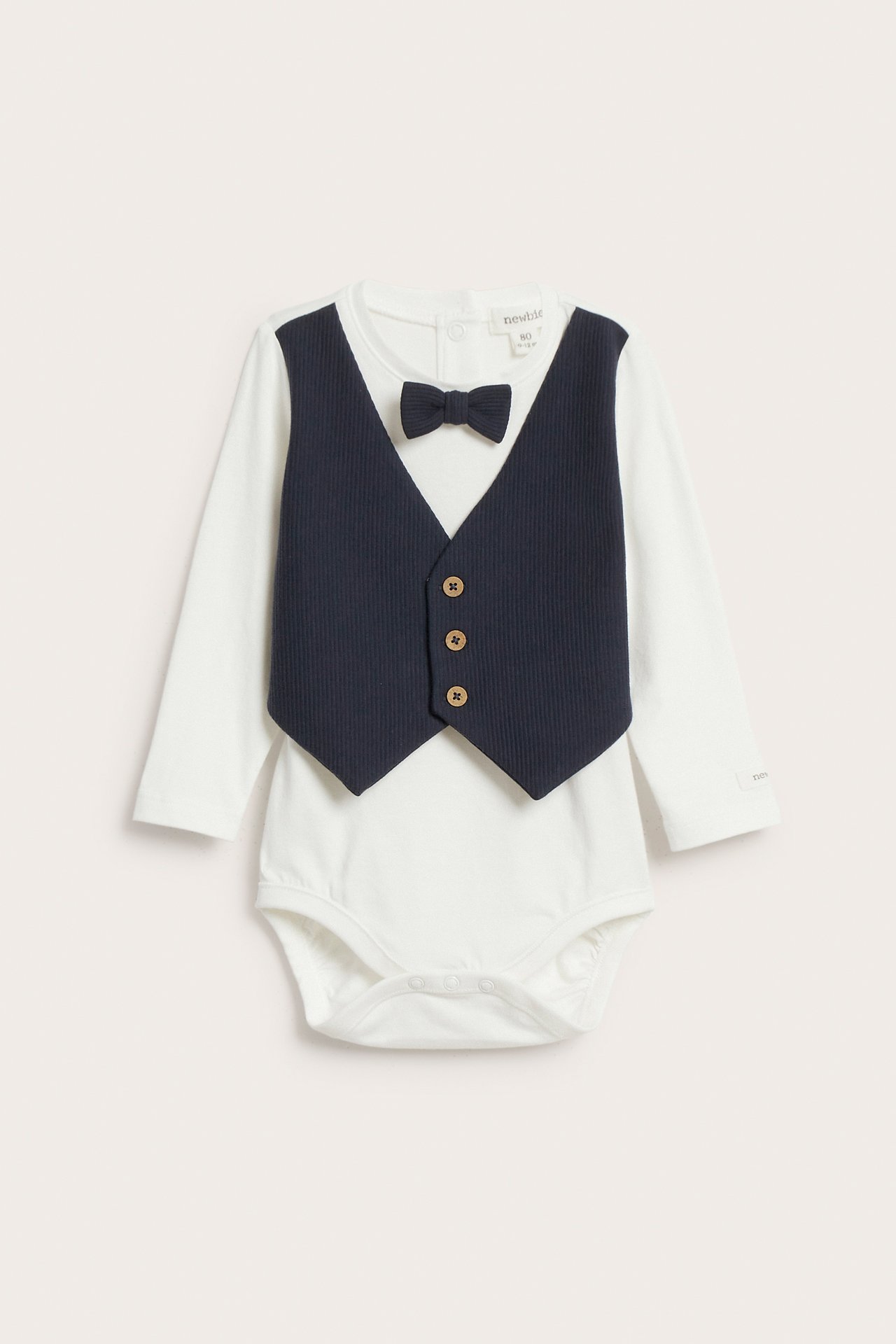 Front view of a baby's off-white cotton bodysuit with an attached dark blue ribbed vest and matching bow tie.
