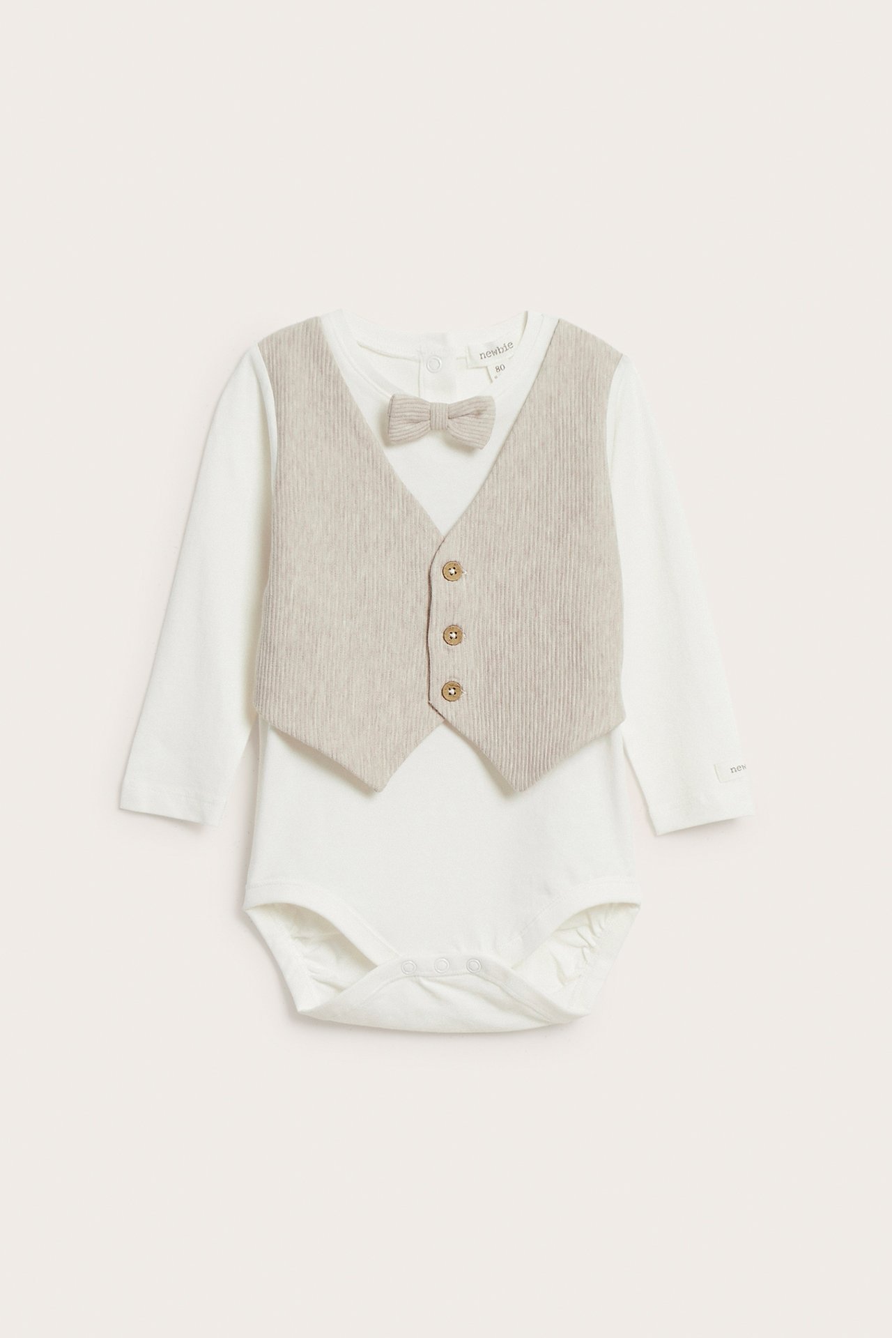 Front view: Baby's off-white long-sleeved bodysuit with attached beige ribbed vest and bow tie, with snaps.