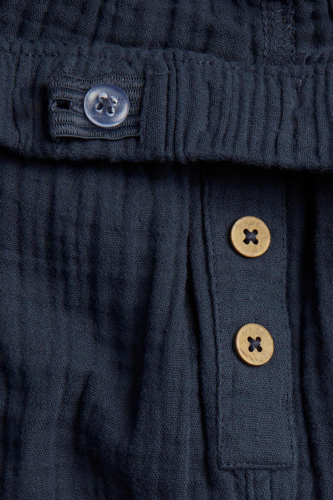 Nahaufnahme einer dunkelblauen Baumwoll-Musselin-Hose mit verstellbarem Bundknopf und zwei dekorativen Frontknöpfen.