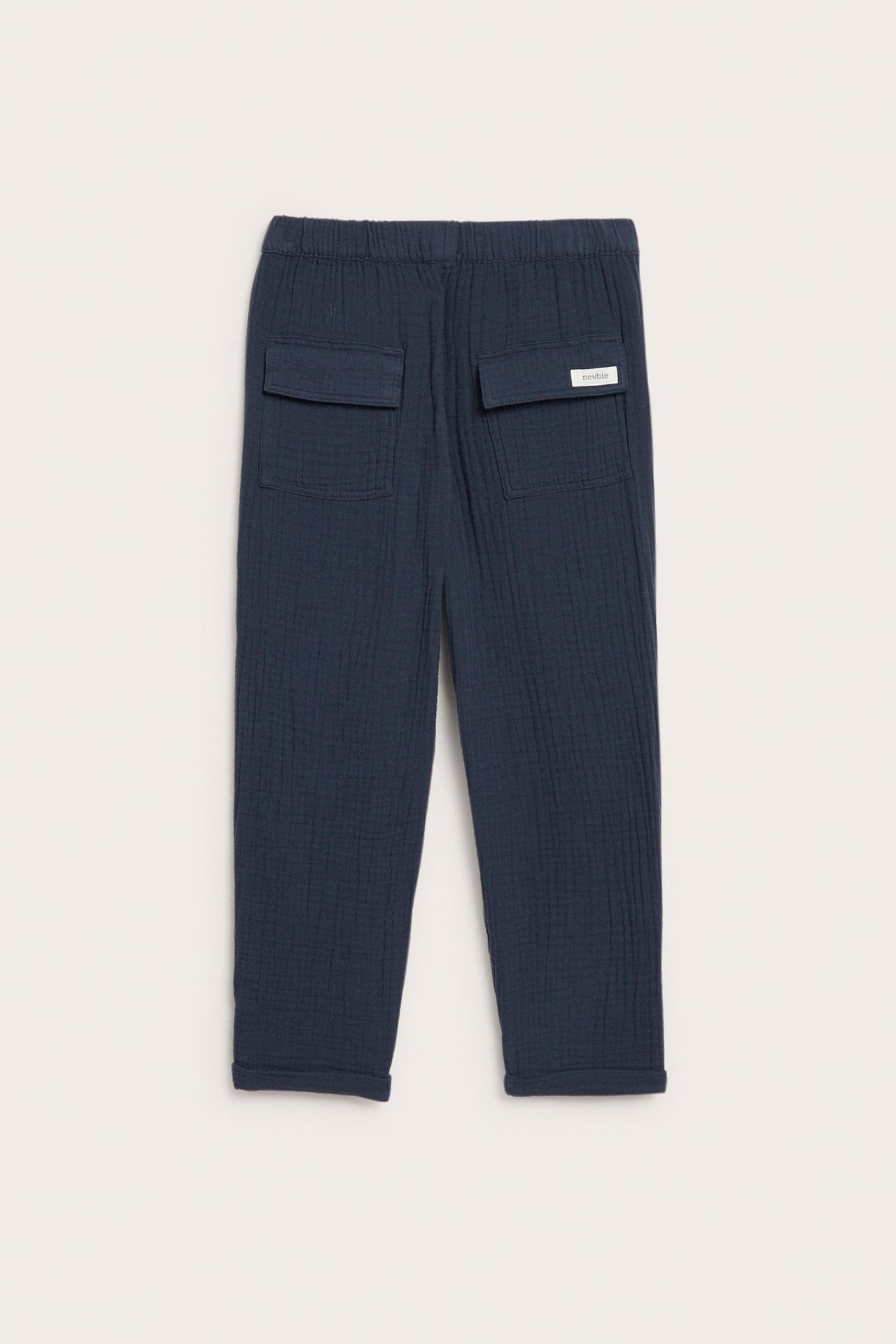 Rückenansicht: Dunkelblaue Baumwoll-Musselin-Hose für Kinder mit Elastikbund, aufgesetzten Gesäßtaschen und umgekrempelten Beinabschlüssen.