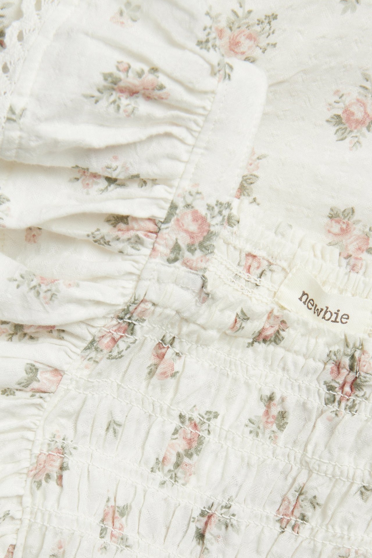 Nahaufnahme eines cremefarbenen geblümten gewebten Jumpsuits mit rosa Rosen, Smokgummi, Rüschen und Spitze.