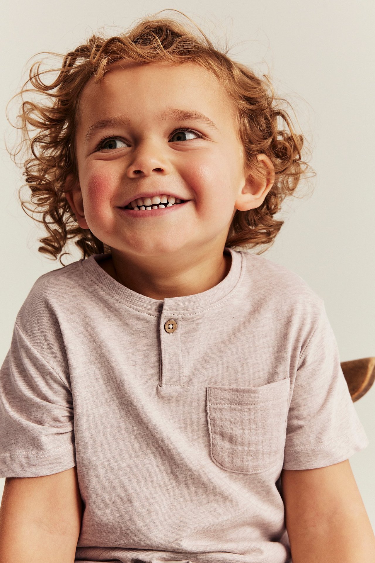 Nahaufnahme, Vorderansicht: Kind in meliertem beige Kurzarm-T-Shirt mit Knopfleiste und Brusttasche.