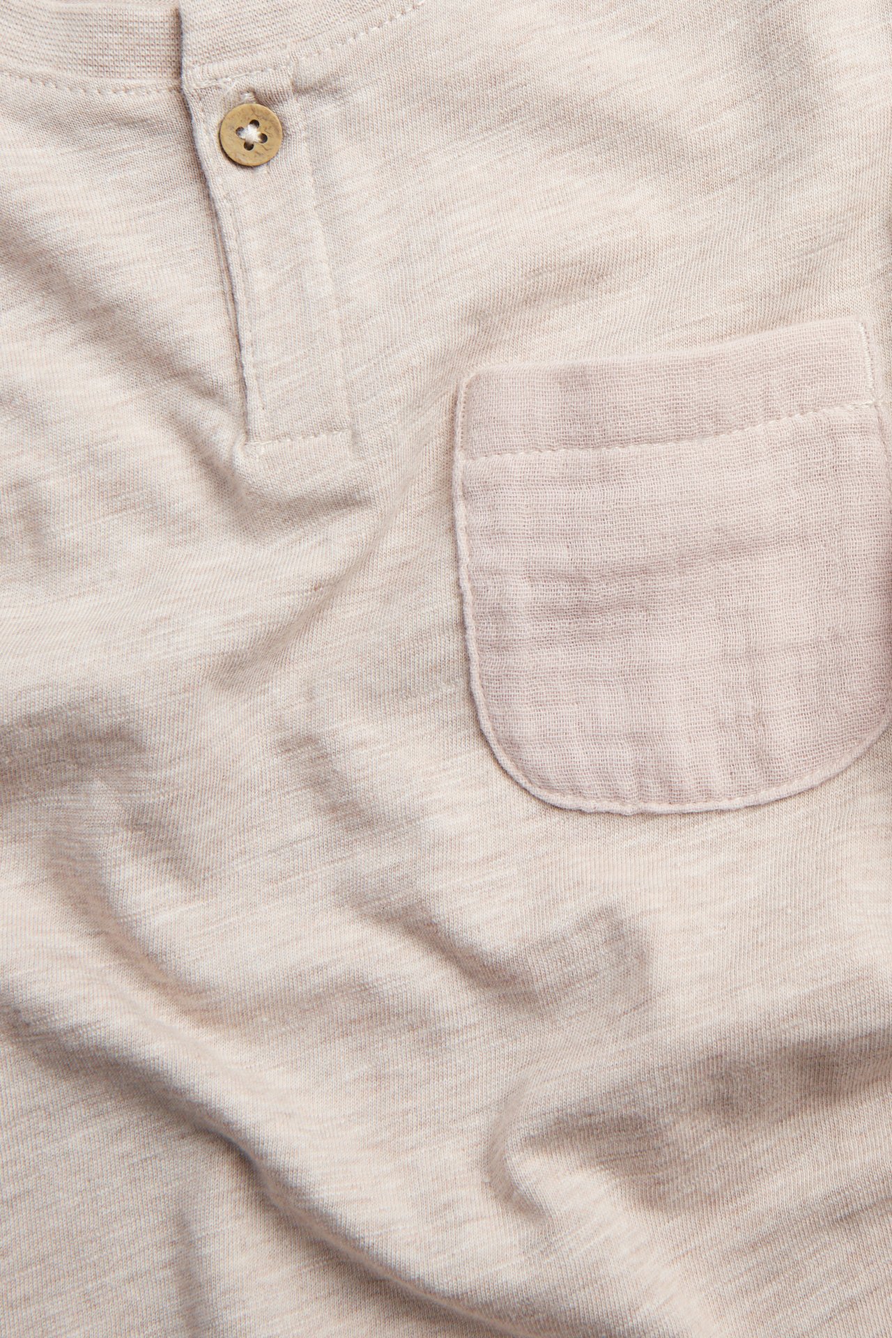Close-up of a melange beige slub jersey T-shirt with a functional button and woven chest pocket.