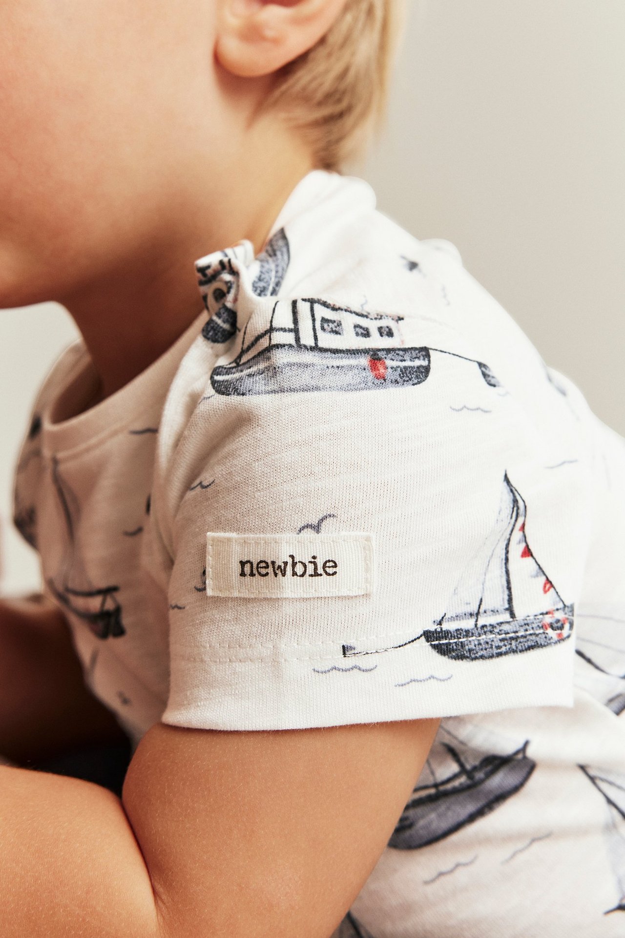 Close-up side view of a kid wearing an off-white short-sleeved cotton bodysuit with a gray sailboat pattern.
