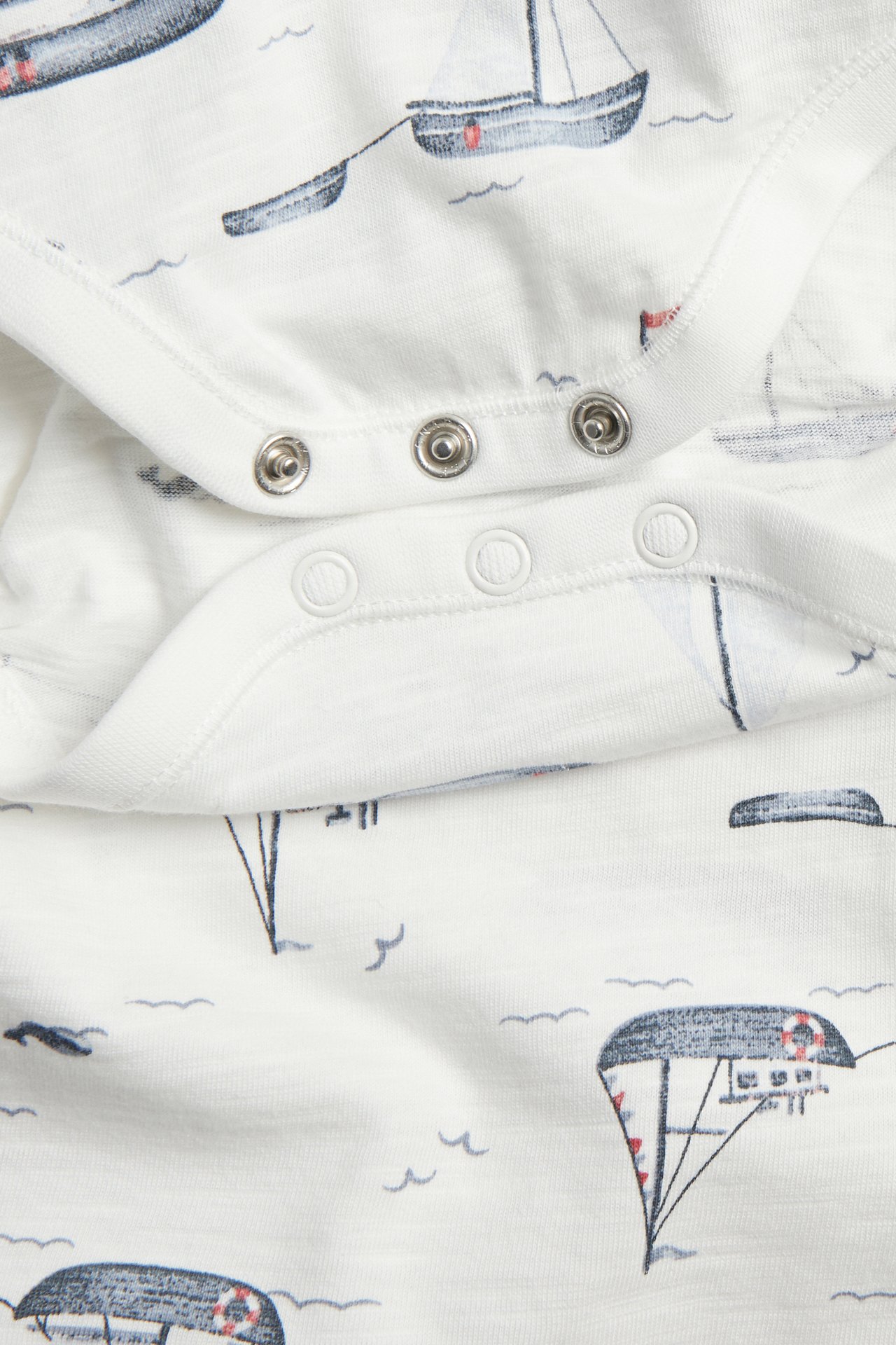 Nahaufnahme eines cremefarbenen Baby-Bodys mit Segelbootmuster und Druckknöpfen.