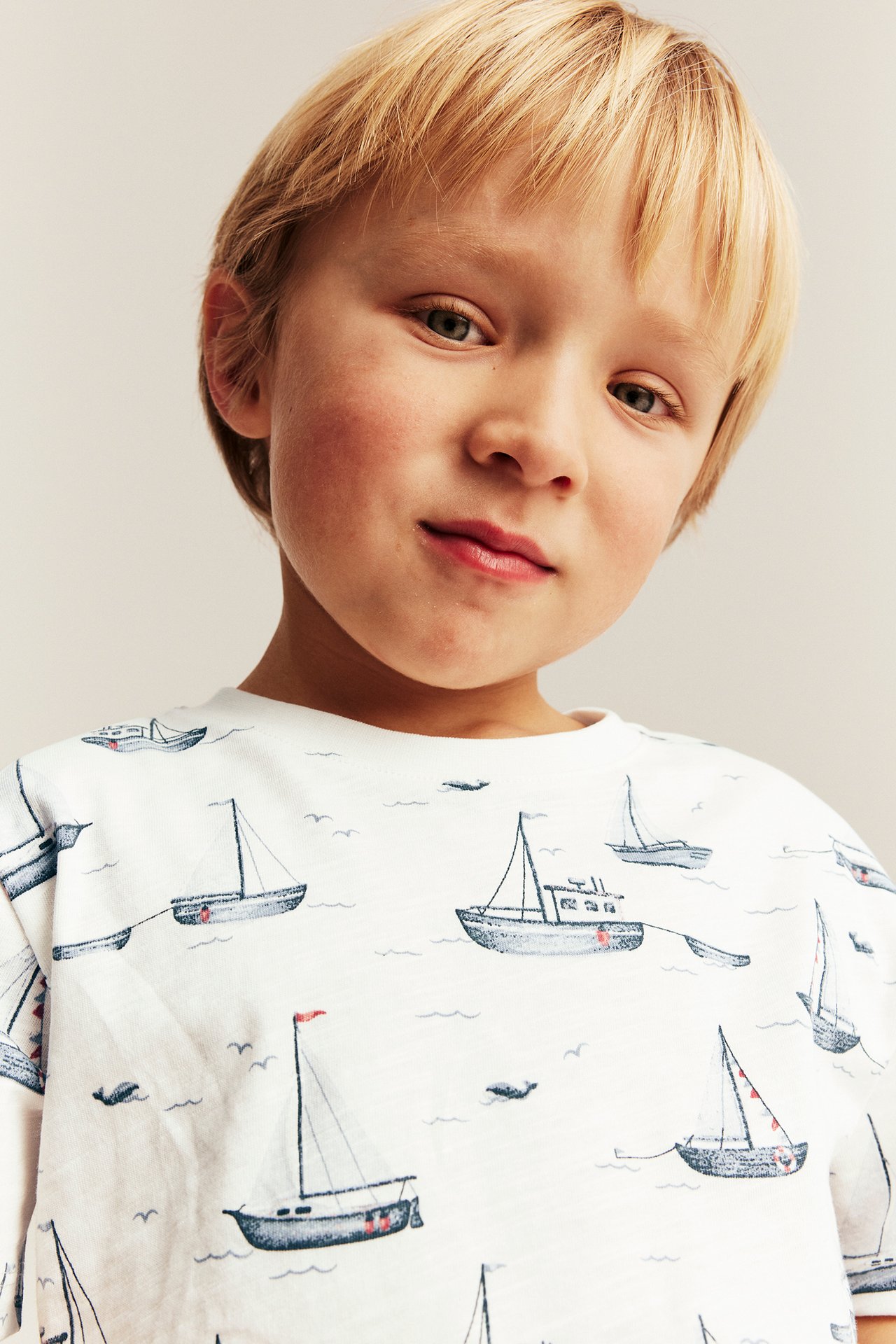 Close-up front view of a kid wearing an off-white slub knit t-shirt with a sailboat pattern.